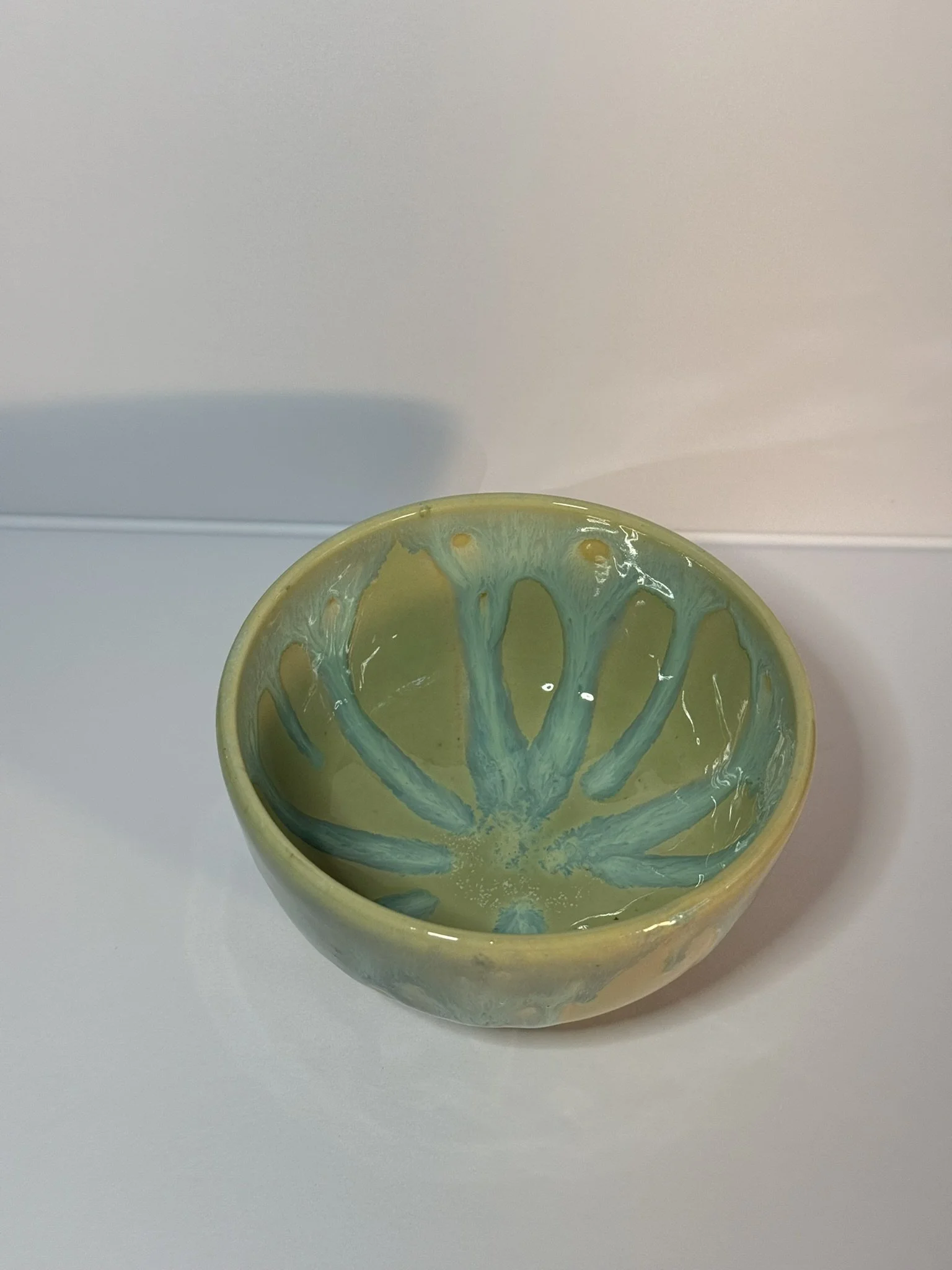 A ceramic bowl with a yellow outer surface and a turquoise and yellow interior, featuring a radial pattern resembling a flower or starburst design.