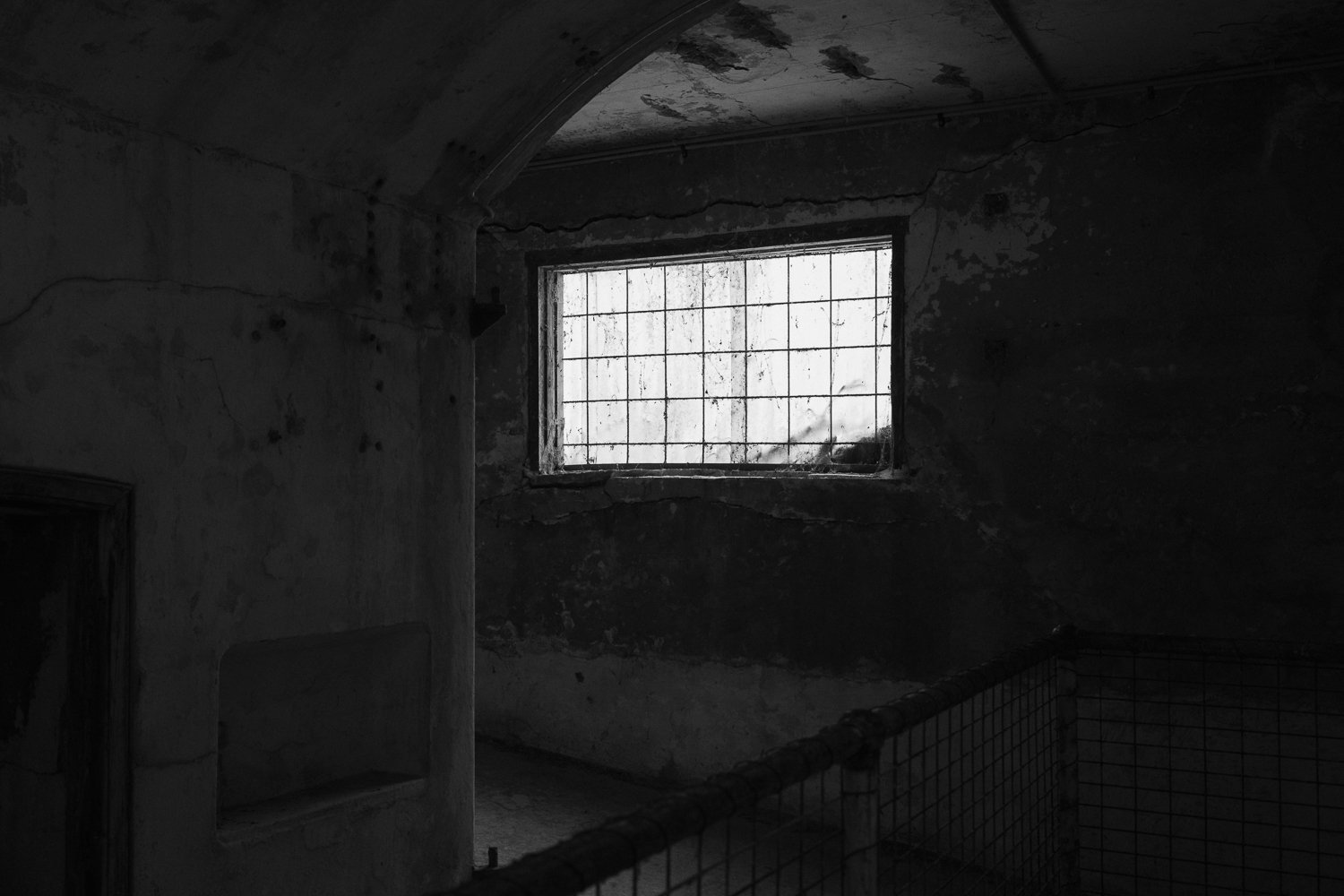 Dark, abandoned room with peeling walls and a barred window letting in some light.