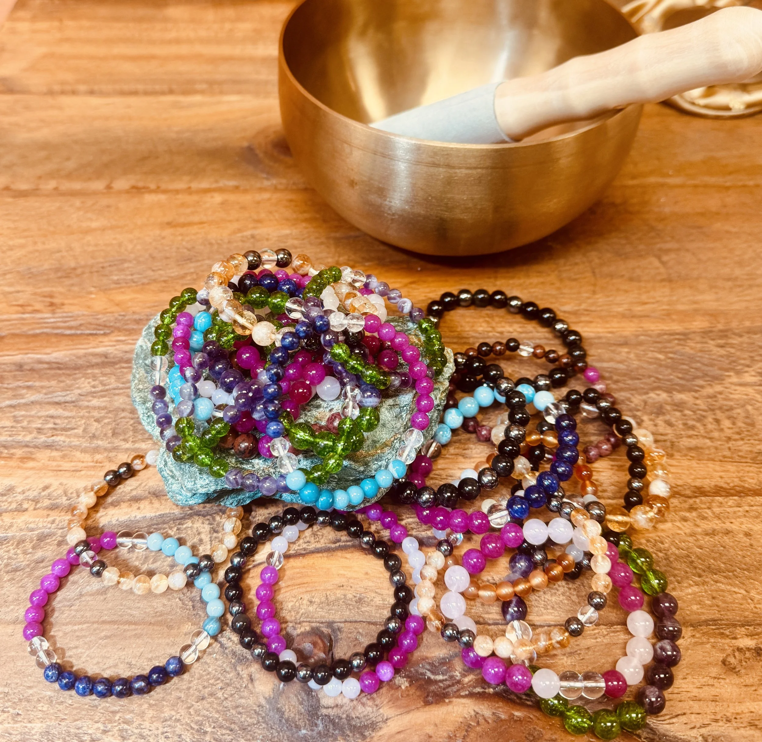Colorful beaded necklaces and bracelets arranged on a wooden surface with a brass bowl in the background.