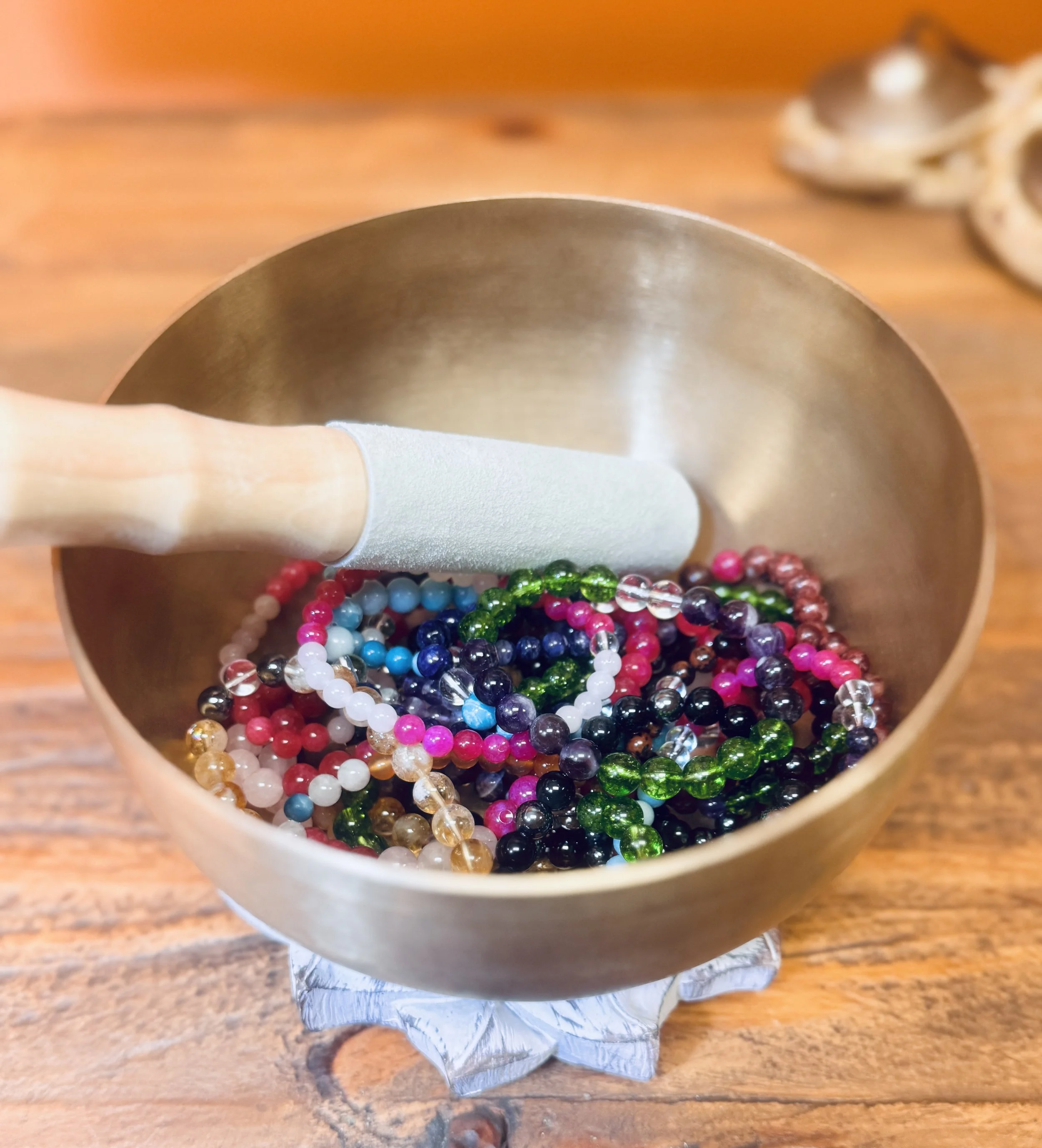 Close-up of colorful gemstone bracelets in a brass singing bowl on a wooden surface.
