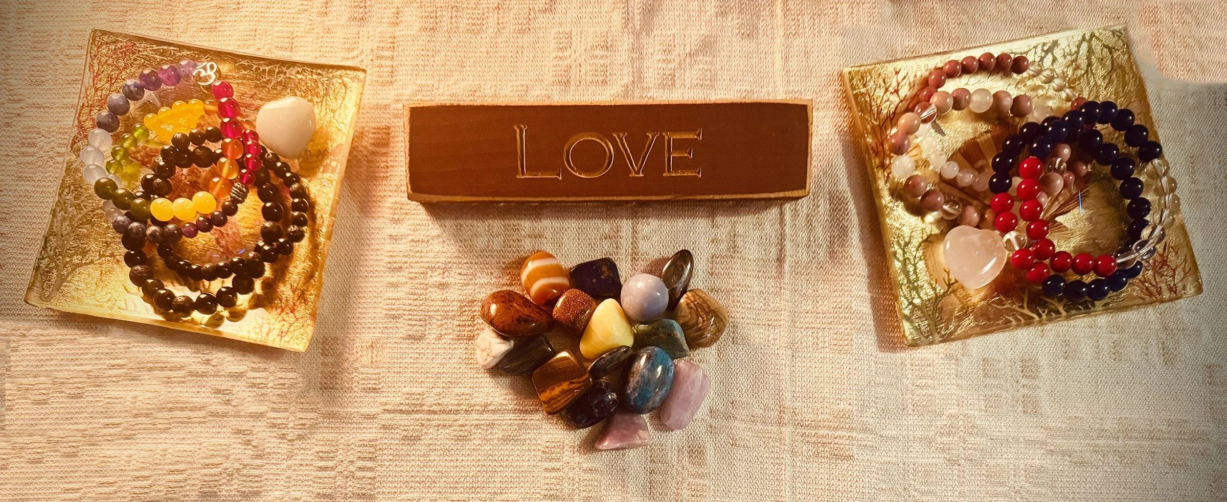 Decorative display with jewelry, stones, and a wooden block engraved with the word 'LOVE' on a pink tablecloth.