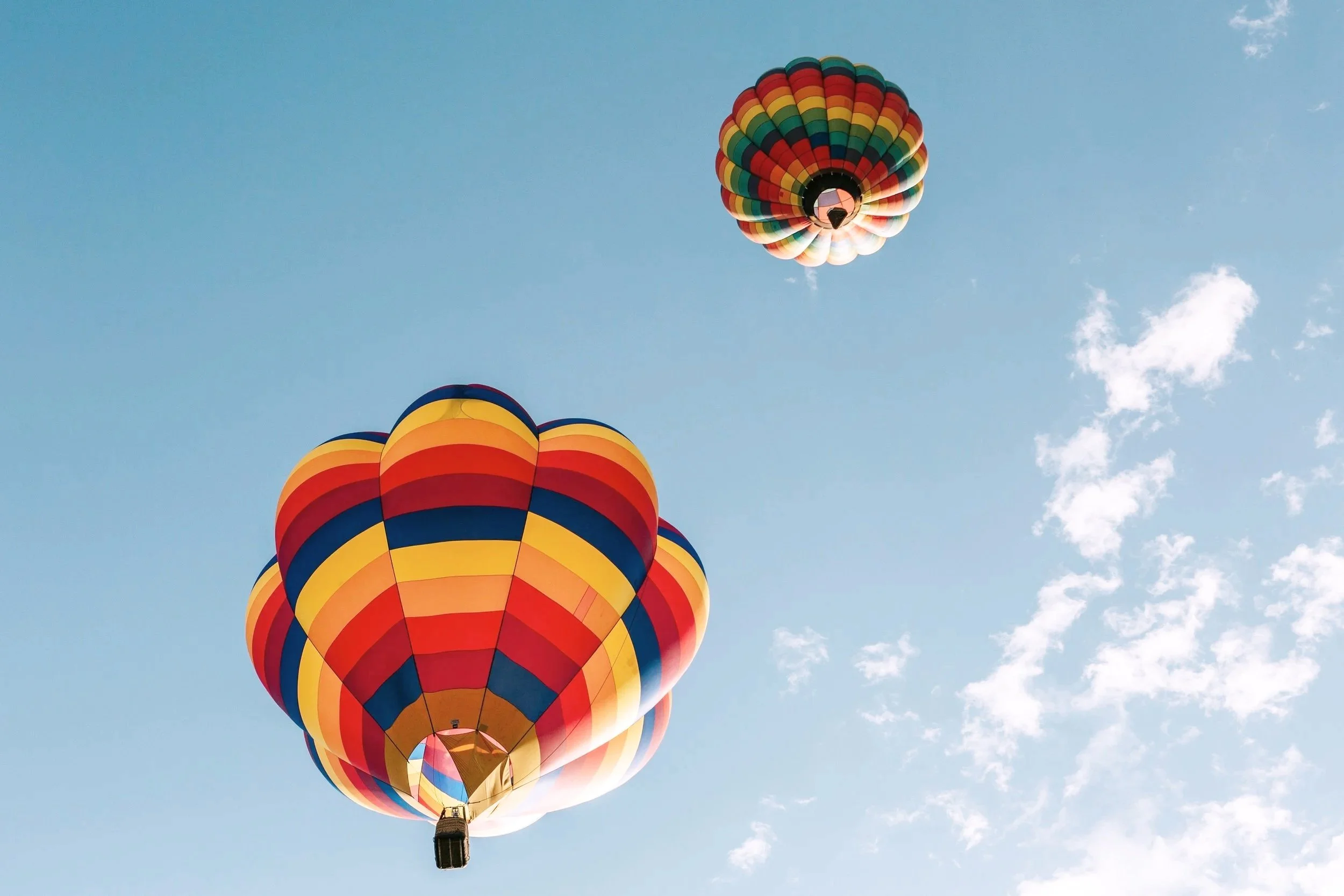 Two colorful hot air balloons flying in a clear blue sky with some clouds.