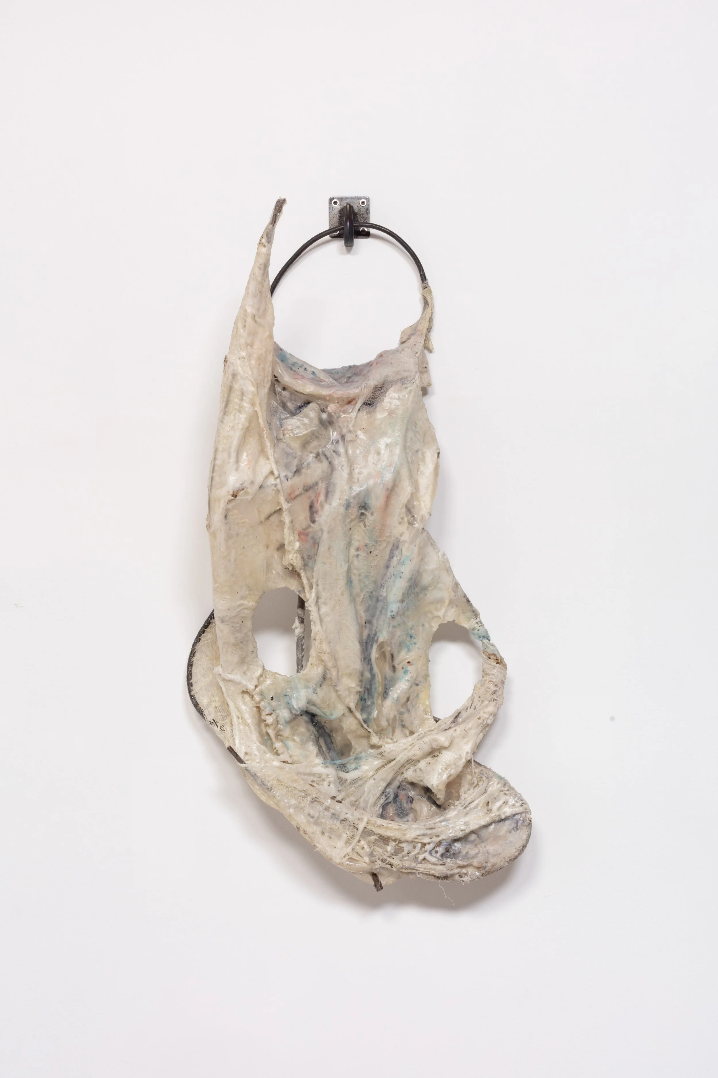 A crumpled piece of clothing, possibly a shirt, hanging on a black metal hook against a plain white wall.