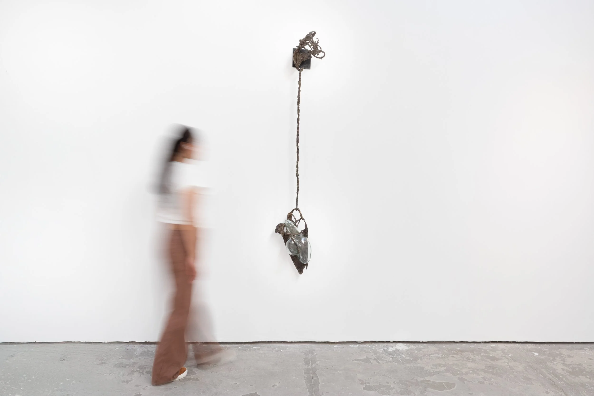 A person walking past an art sculpture on a plain white gallery wall.
