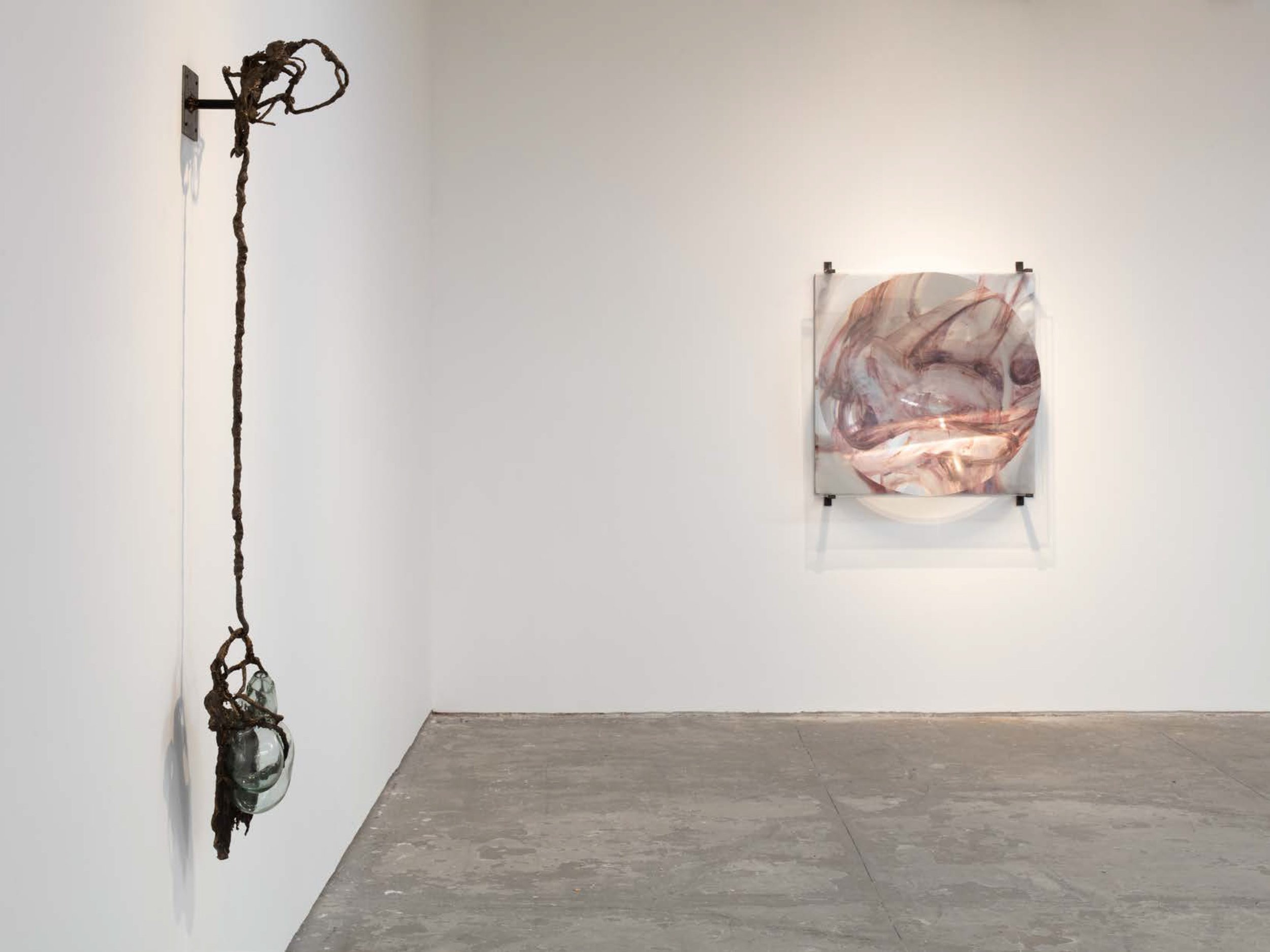 Contemporary art gallery with a white wall displaying a twisted, vine-like sculpture on the left and an abstract pink and gray painting on the right.