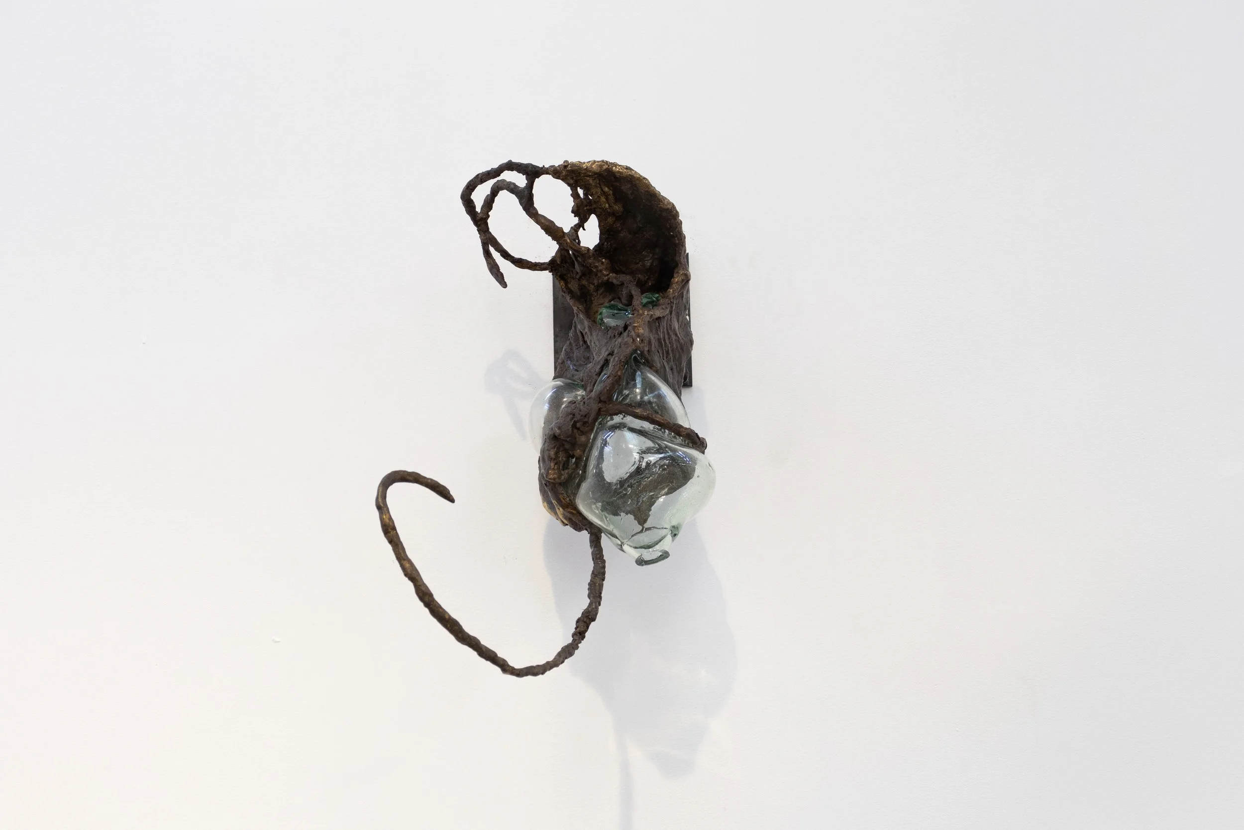 An art installation featuring a driftwood sculpture with a glass orb and small green marble on a white background.