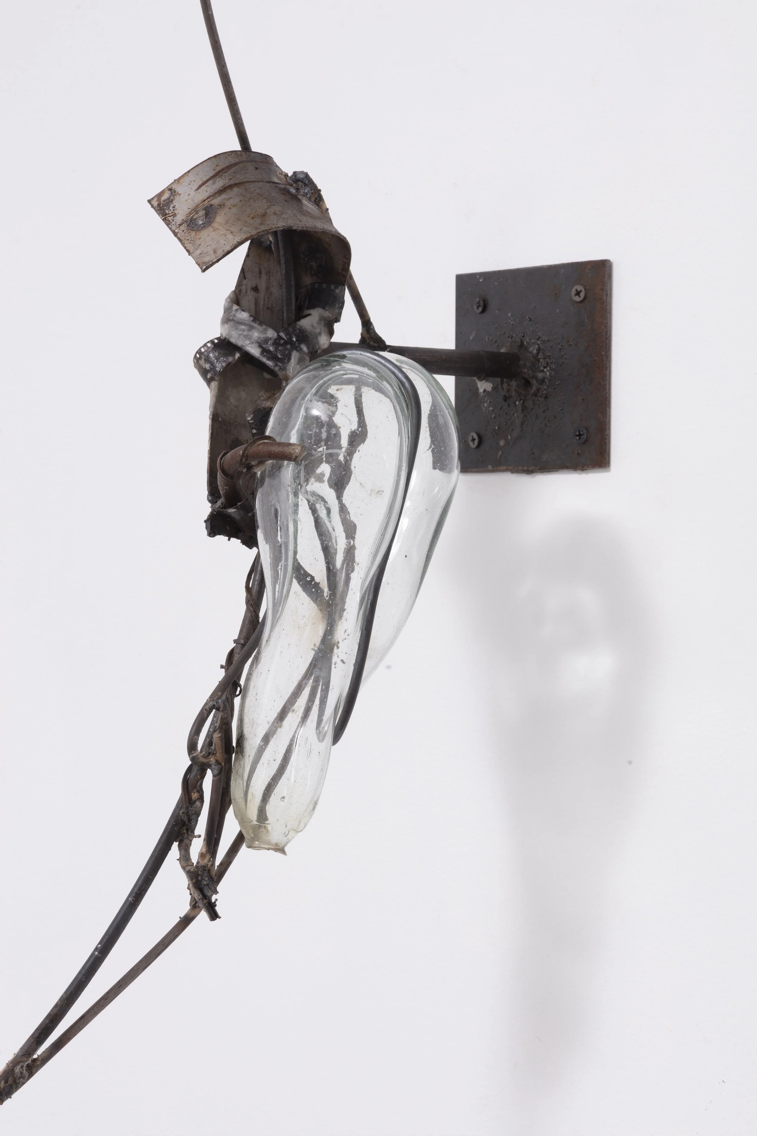 A rusted, broken elevator light fixture with exposed wires, mounted on a white wall.