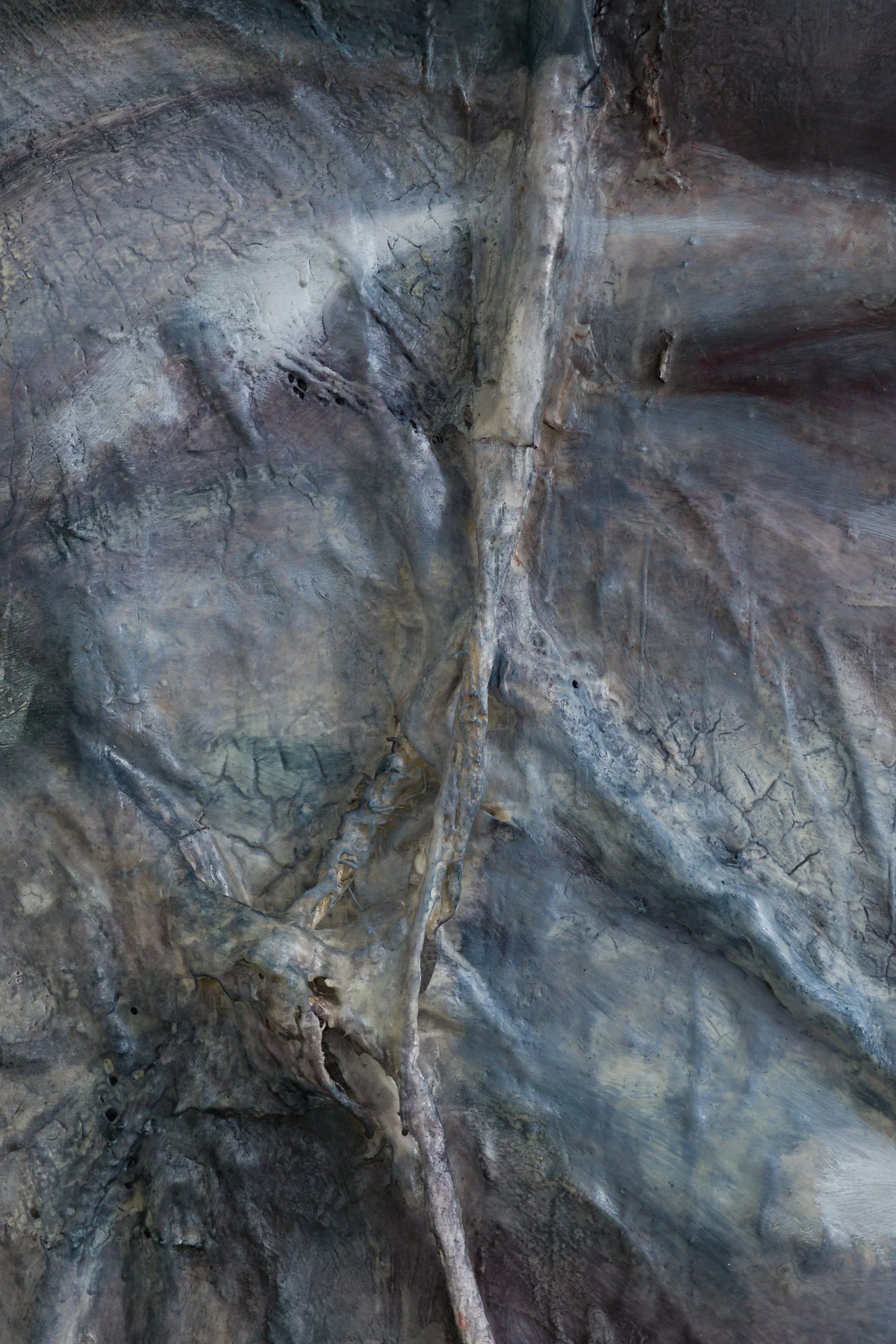 Close-up of a textured, rocky surface of a painting with various shades of gray, brown,Close-up of a rock wall with a prominent, twisted, and weathered tree root or branch extending across the surface, showing textures and shades of gray and brown.