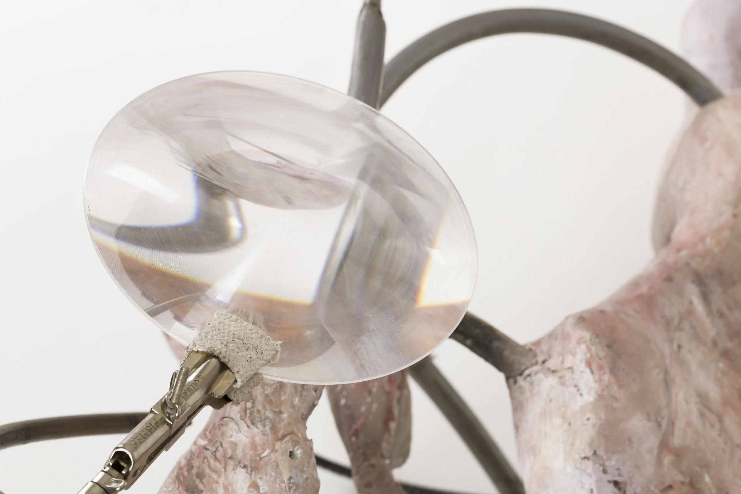 Close-up of a glass object being held by a gloved hand, with a metal clamp attached at the bottom.