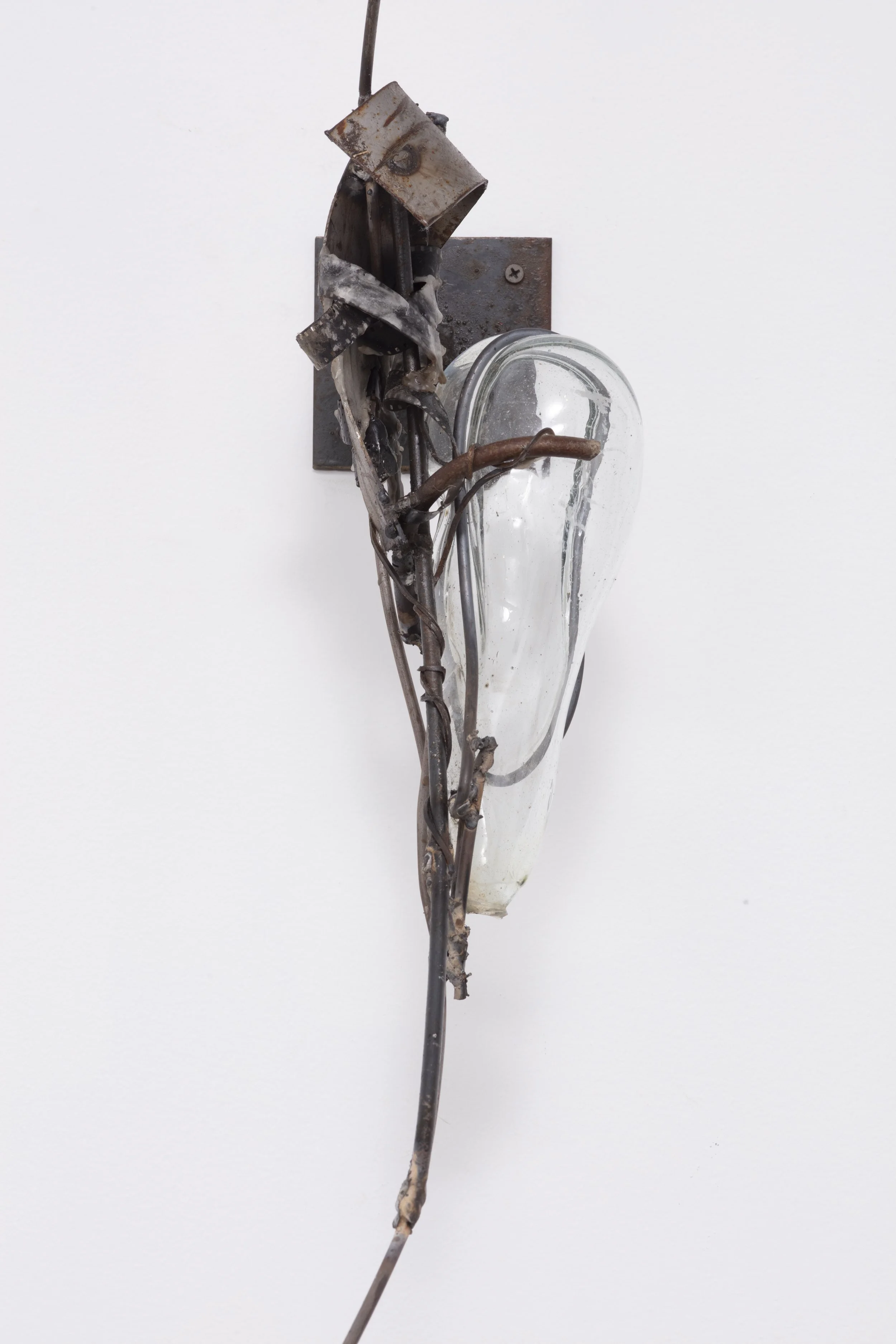 Art installation resembling a human heart made from found metal and glass, mounted on a white wall.