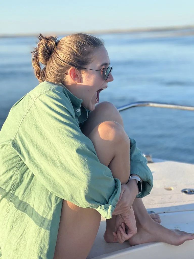 A woman sitting on a boat by the water, expressing surprise or excitement.