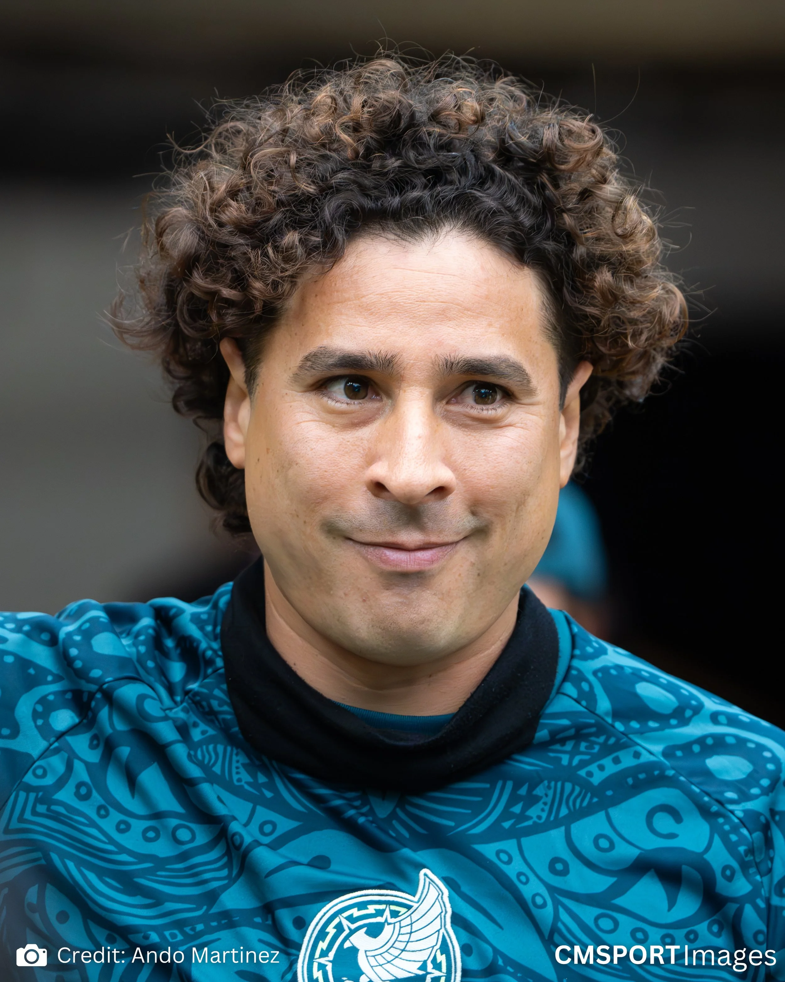 A man with curly hair wearing a blue sports jersey with a Polynesian-style pattern.