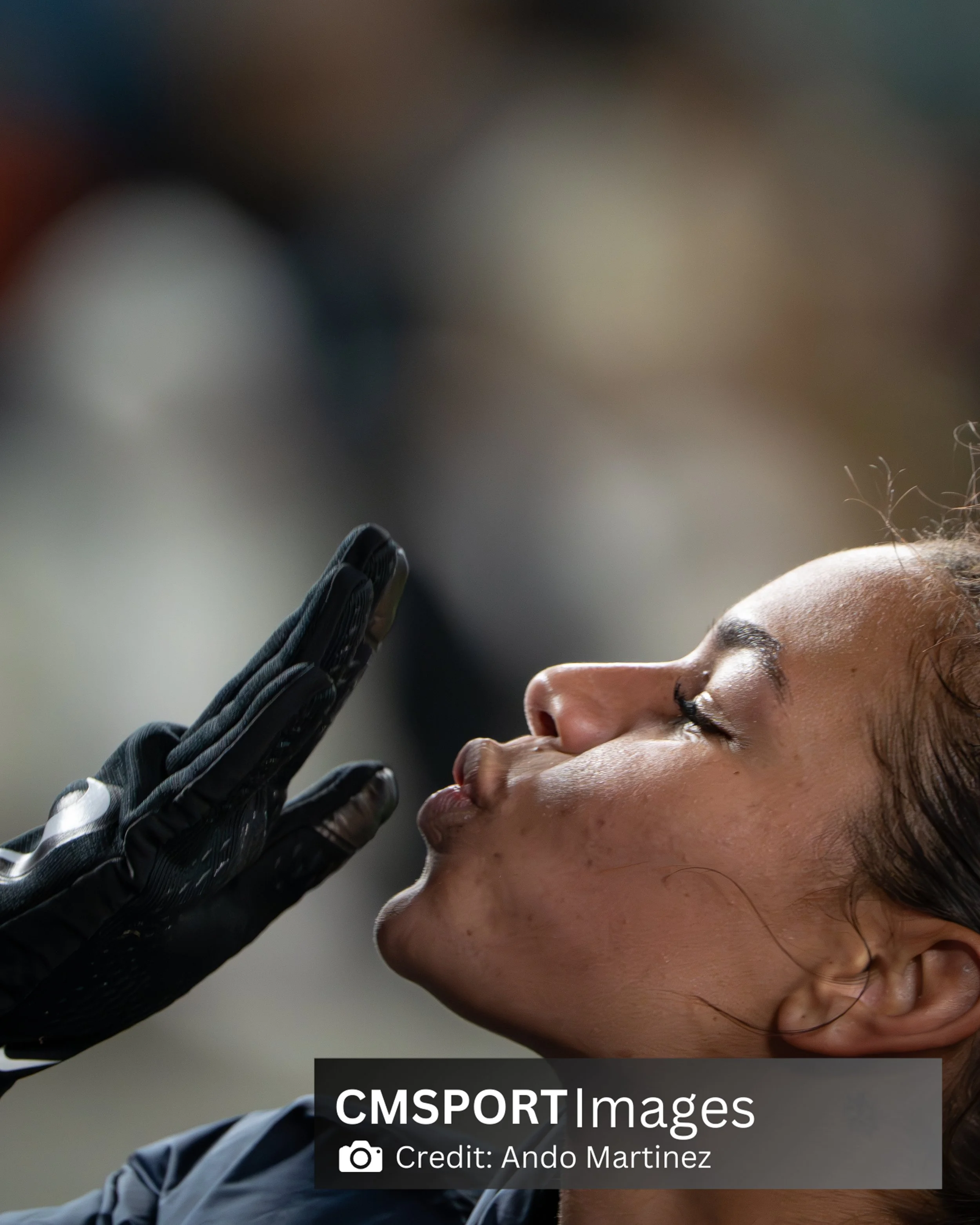 A female athlete in sports gear blowing a kiss or giving a farewell gesture with her hand, with her eyes closed.