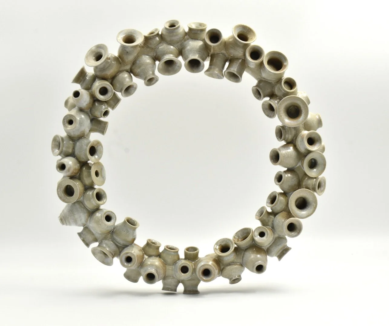 A circular sculpture made of numerous small, beige ceramic pots arranged in a ring.