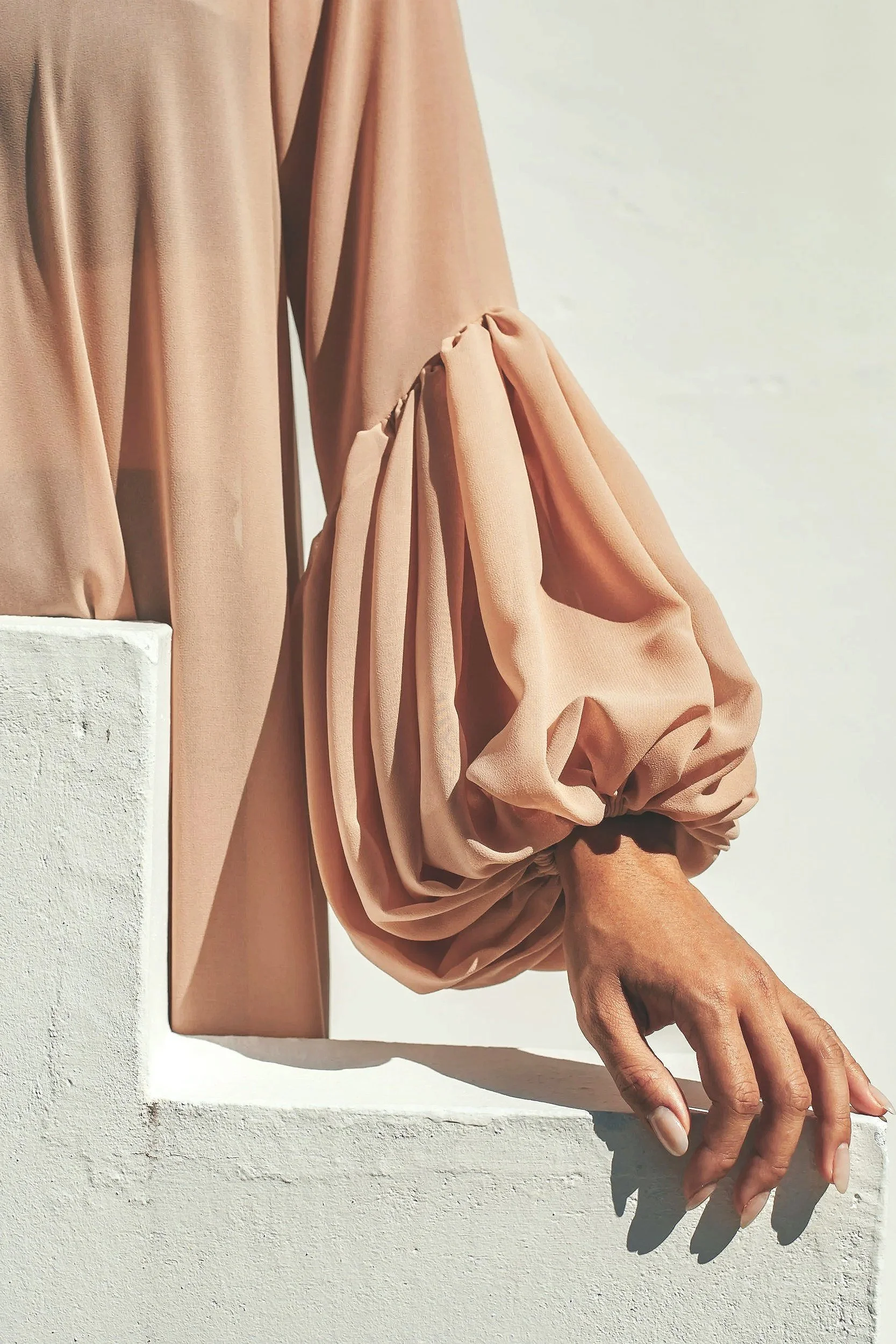 A person's hand resting on a white ledge, wearing a flowy, long-sleeved top with puffed sleeves in a beige color.