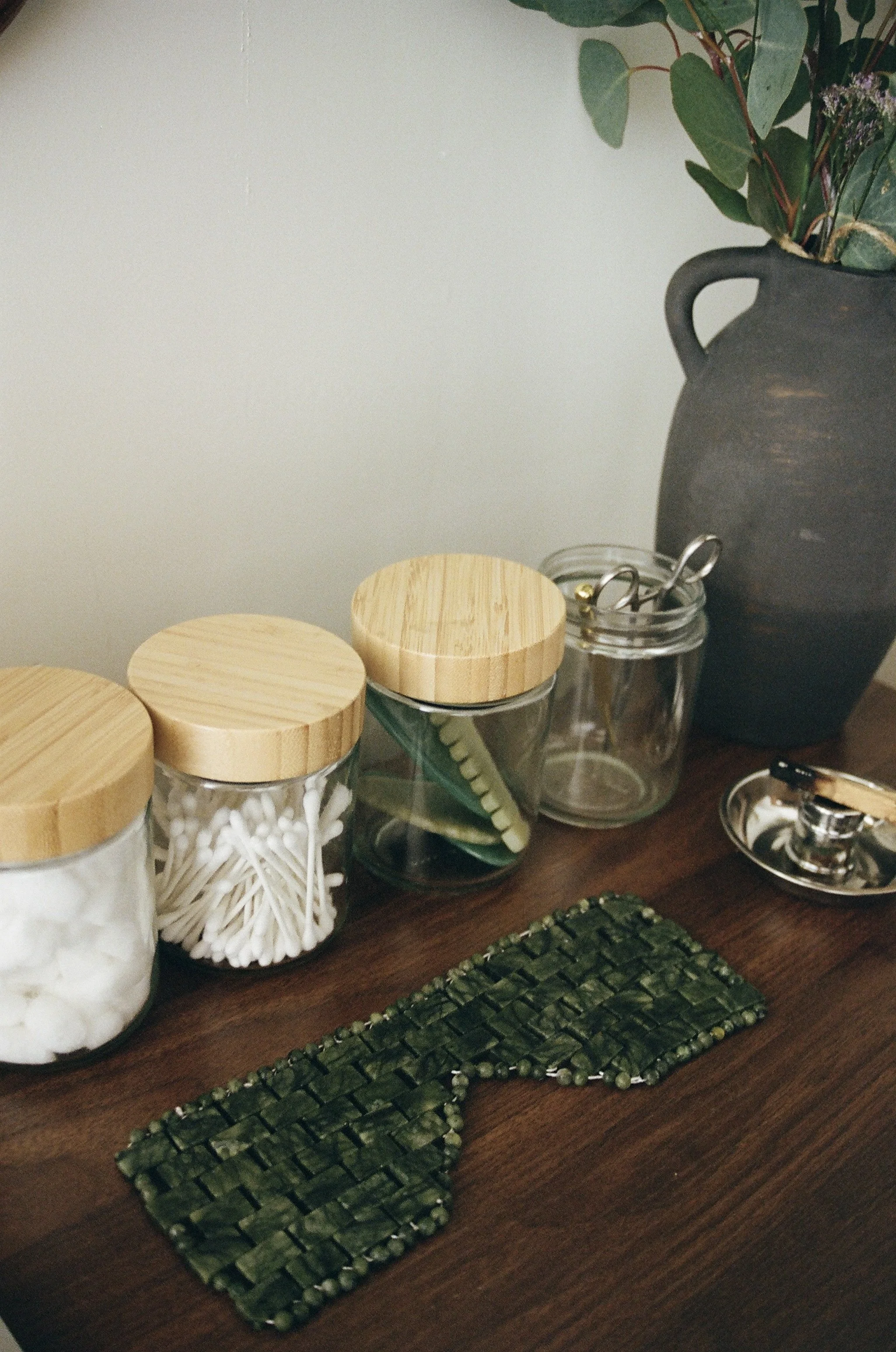 Decorative jars with wooden lids and vases with green leaves on a wooden table.