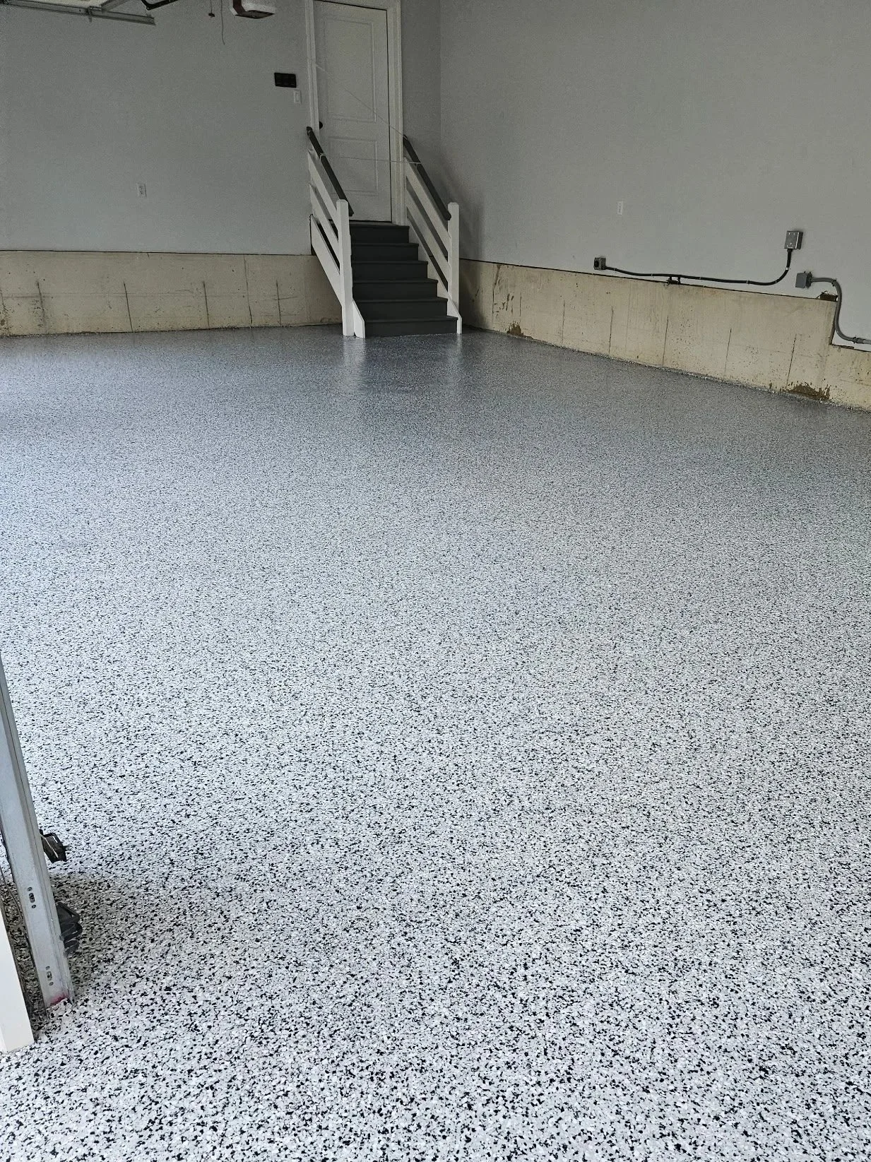 A polished concrete floor with a colorful abstract swirl pattern in shades of black, white, pink, and copper in a room with brick walls and utility fixtures.
