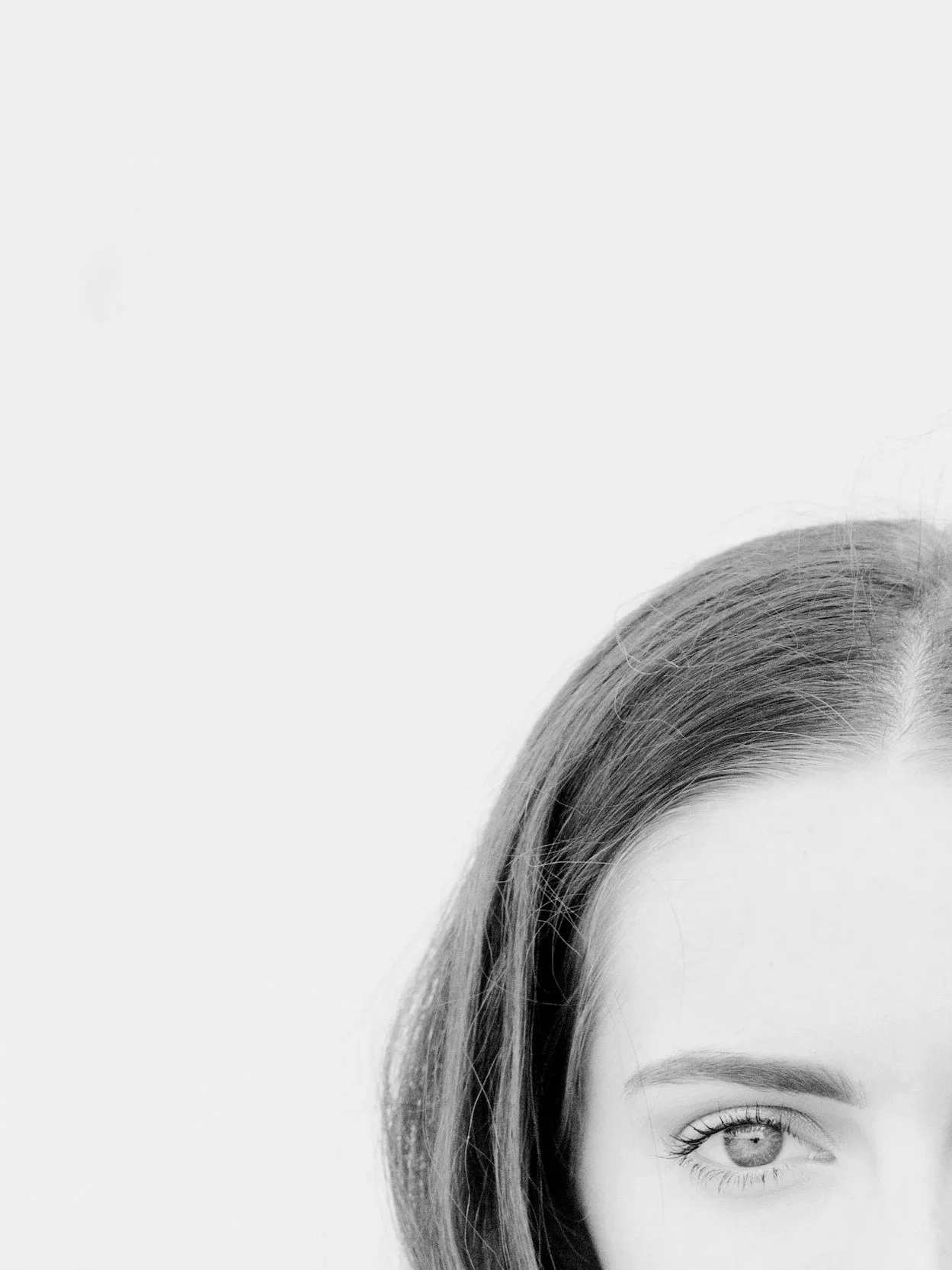 Close-up of a young woman's face, focusing on her left eye, with part of her forehead and hair visible, in black and white.