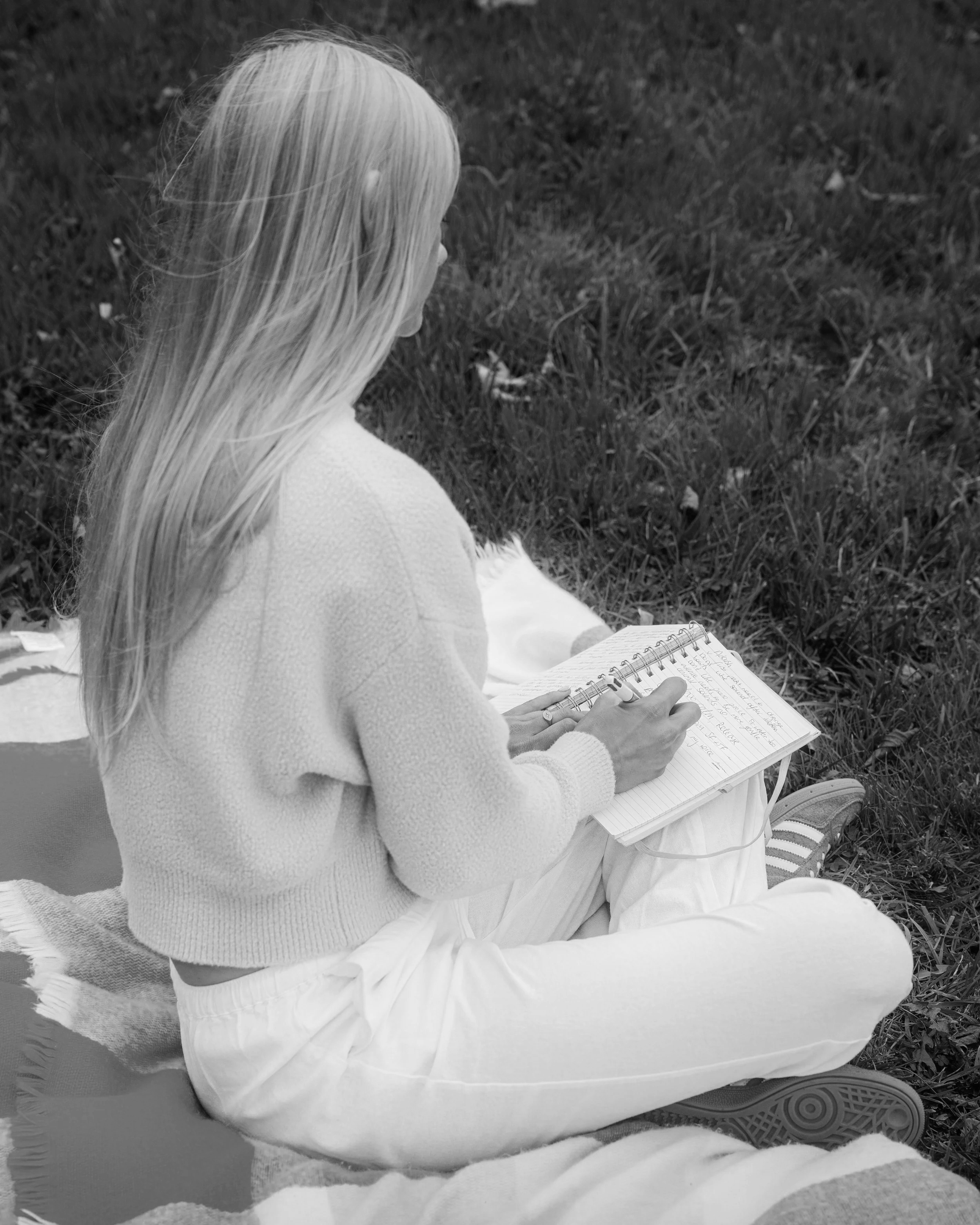 Laura Ann Costello Bio-Energy Therapist sitting on a blanket in a park of Galway, writing in a notebook.