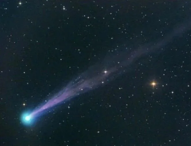 A bright comet with a glowing nucleus and a long, glowing tail streaks through space filled with stars.