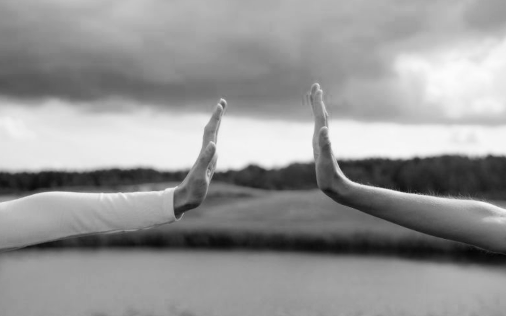 Two people reaching out to each other outdoors, cloudy sky in the background, black and white photo