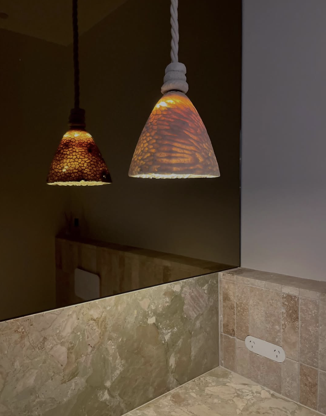 Marovo Island coral pendant light reflecting on a bronze mirror hanging over a marble countertop in a powderoom