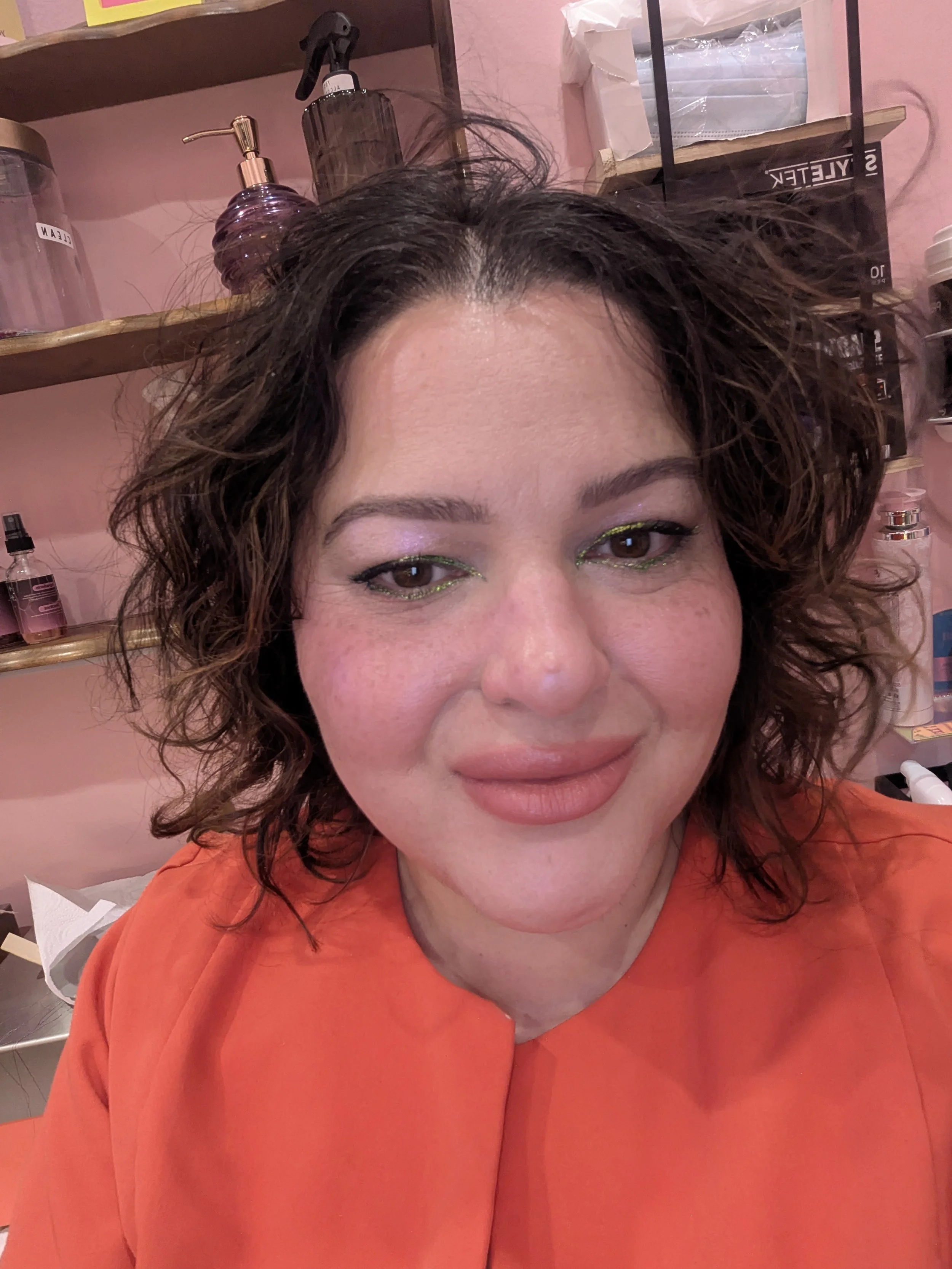 image of woman wearing scrubs, dark curly hair, sparkly glowy make up