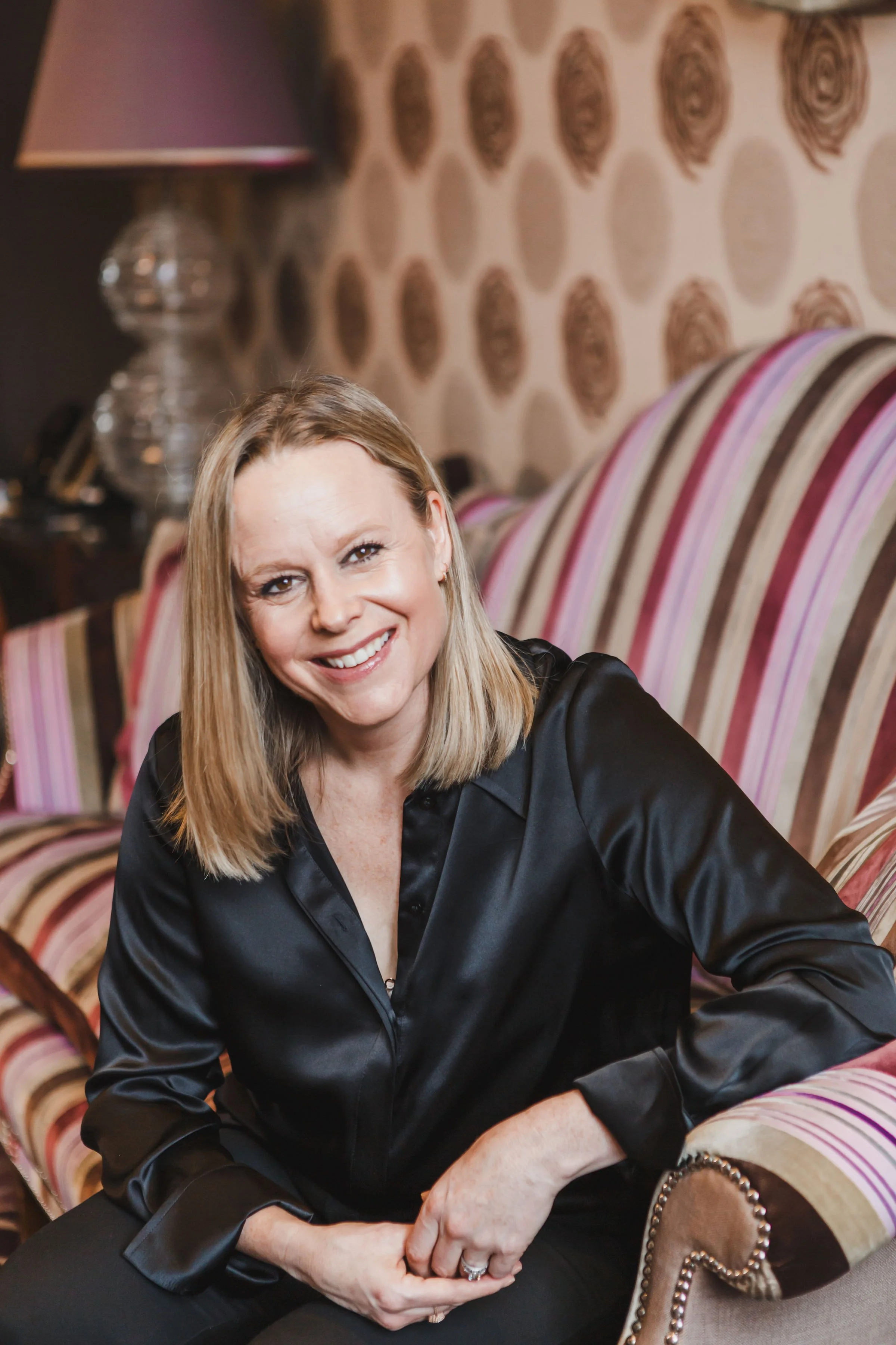 A woman with blonde hair smiling and sitting on a colorful striped sofa in a living room.