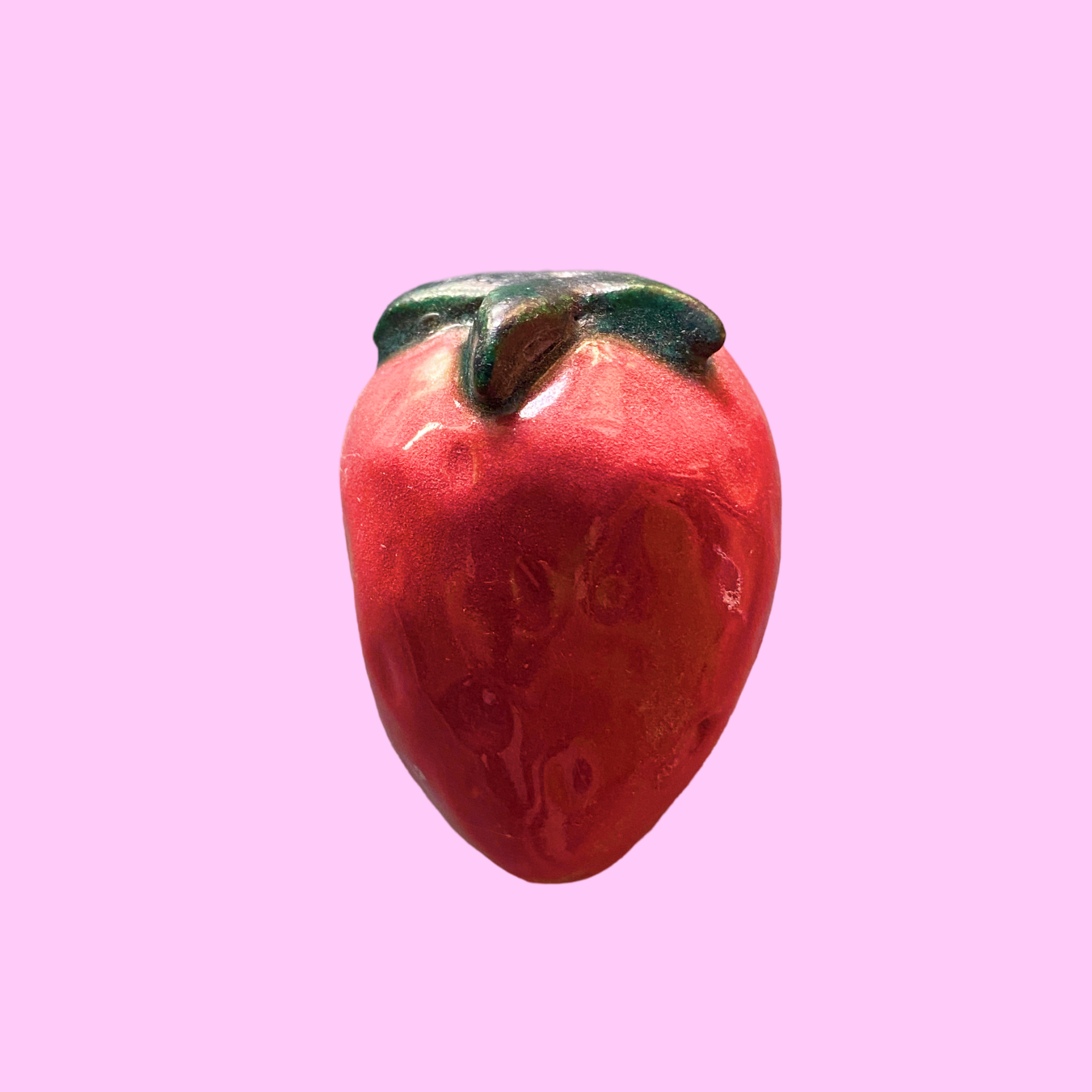 Keramik-jordbær, rød med grøn top på lyserød baggrund.