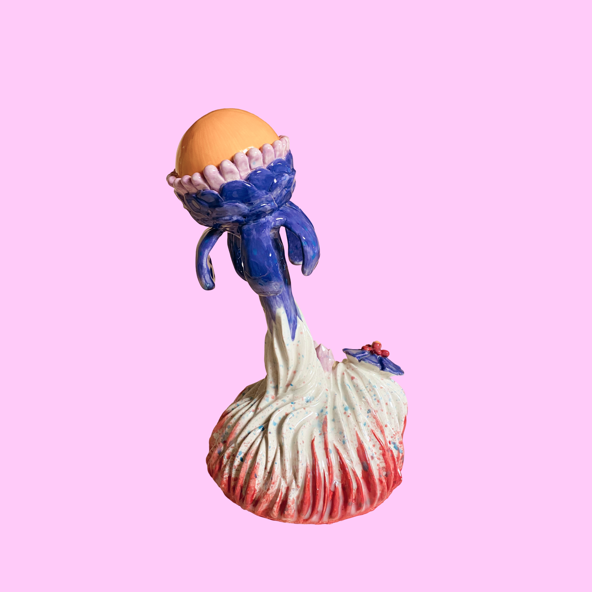 En kunstnerisk skulptur af en vækst med en stor, orange kugle på toppen, omgivet af lilla og lyseblå elementer, stilfuldt og fantasifuldt design, sat mod en lyserød baggrund.