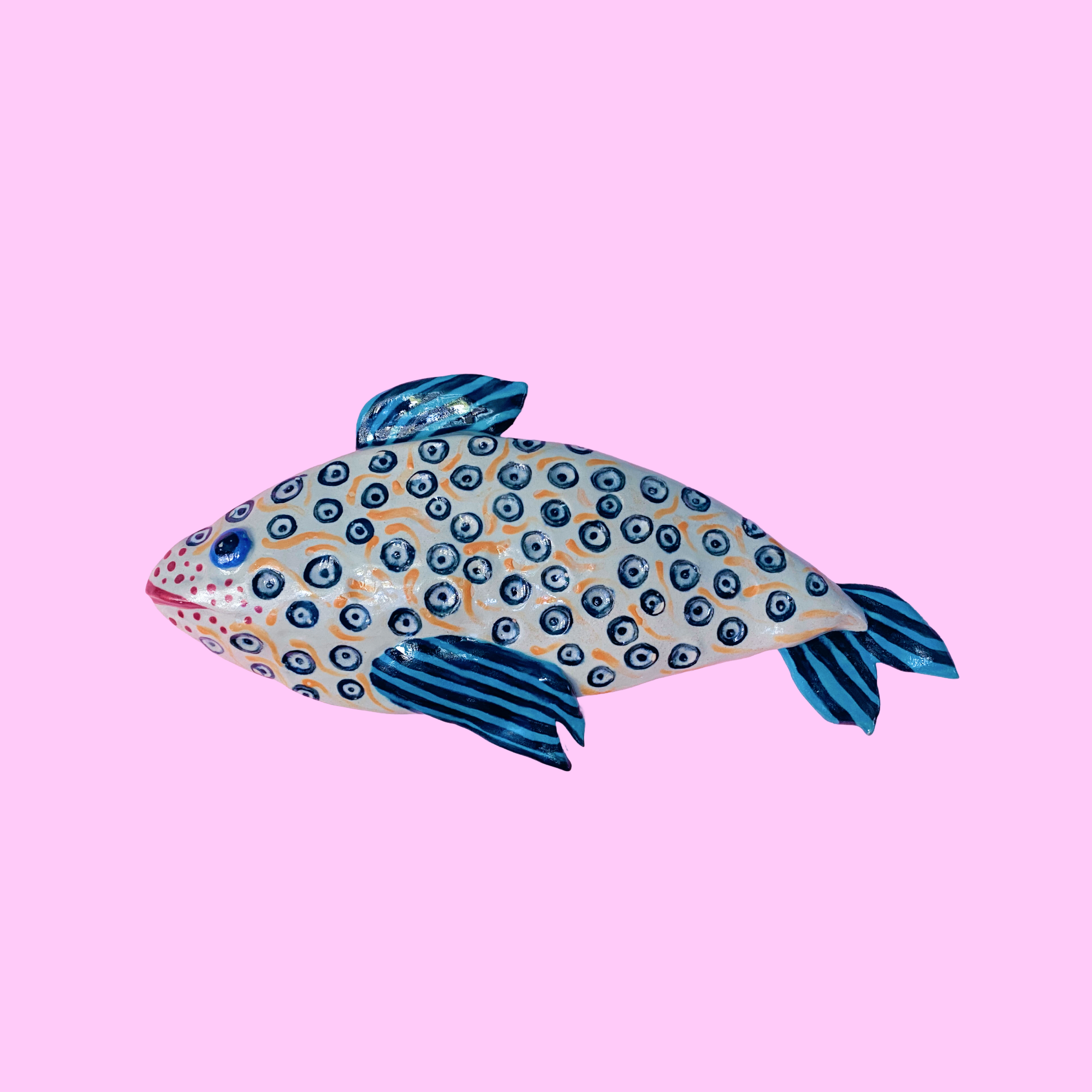 Farverig keramik fisk med blå pletter og striber på en lyserød baggrund.