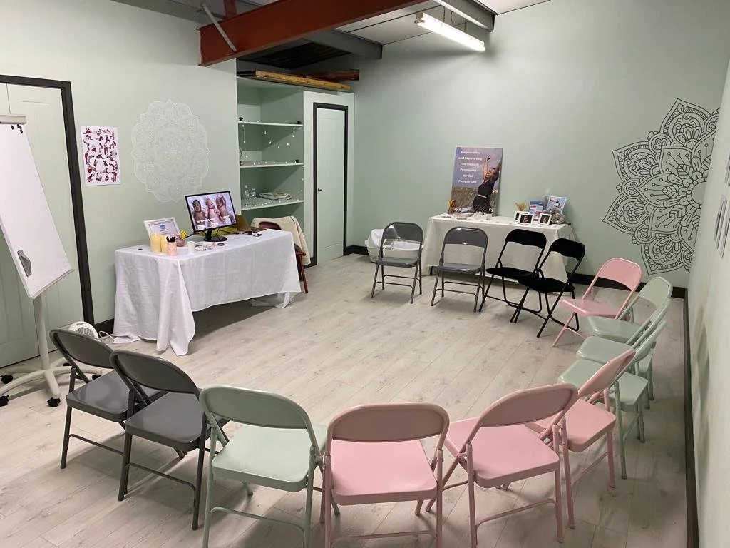 A room set up for a small event or meeting with chairs arranged in a semi-circle, tables with promotional materials, and decorative wall art.