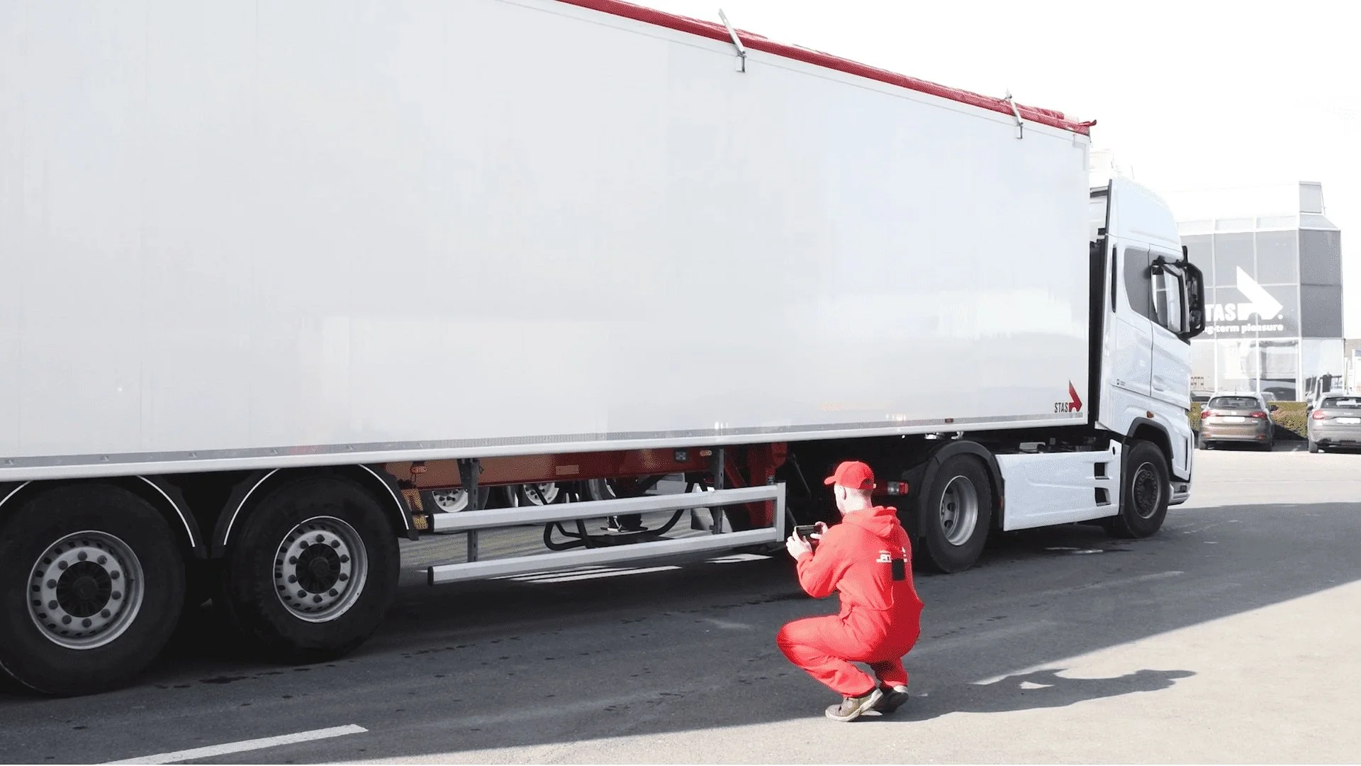 Person in red coveralls taking a photo of a white semi-truck trailer.