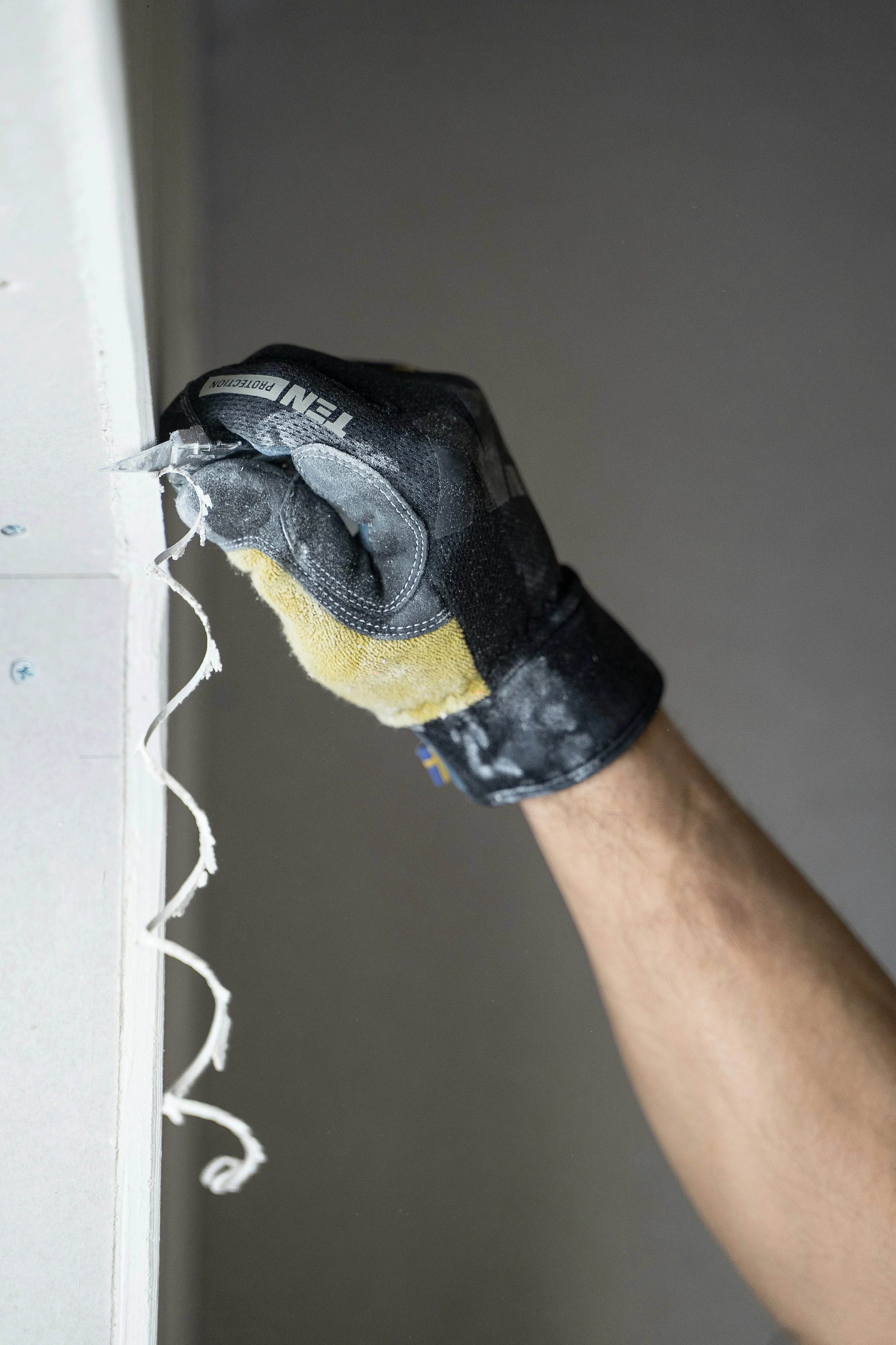 En person med handsker bruger en værktøj til at fjerne et stykke materiale fra en hvid overflade.