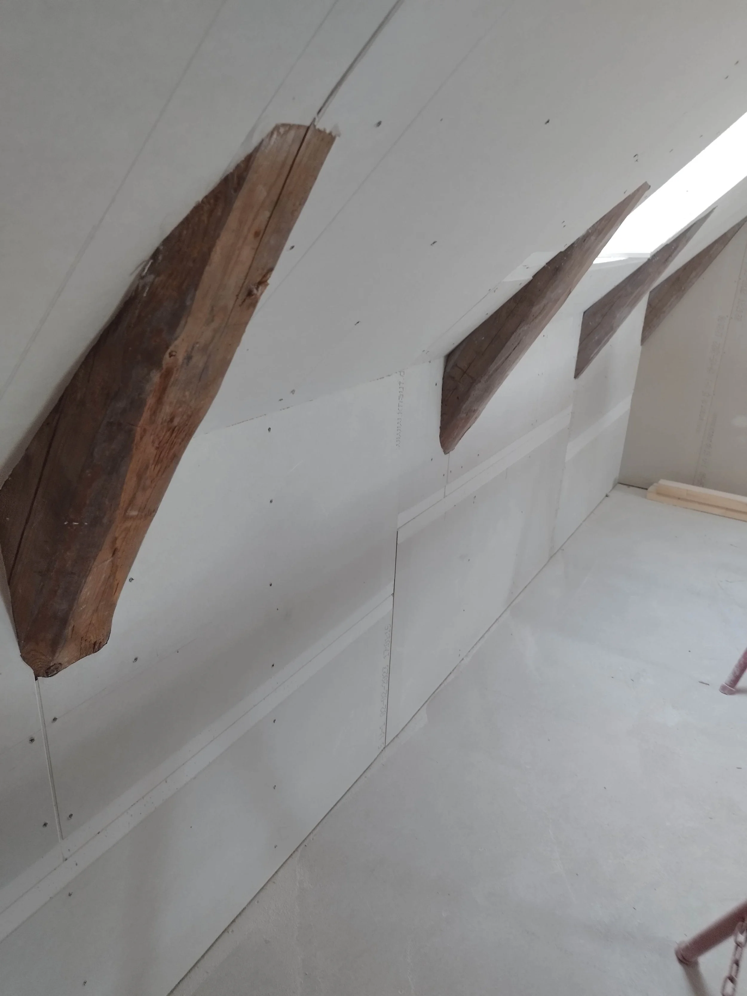 Ufærdigt loft med monterede gipsplader og synlige træbjælker.