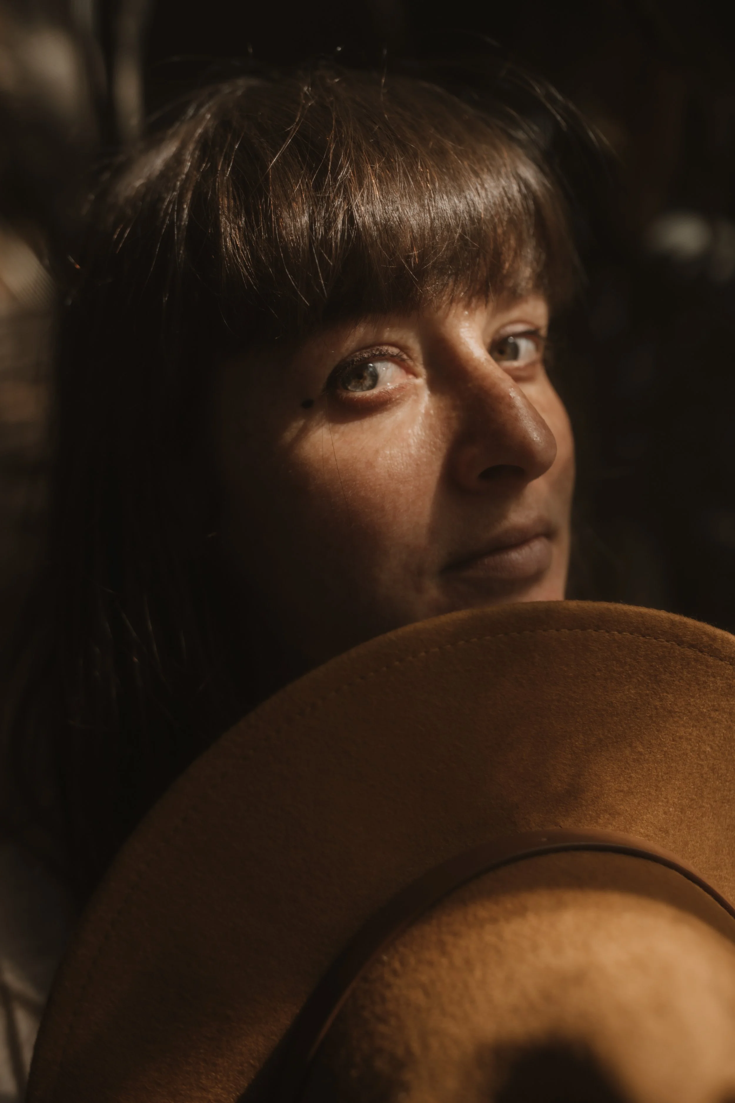 Close-up portrait of a woman with brown hair, partially visible face, and a brown hat.