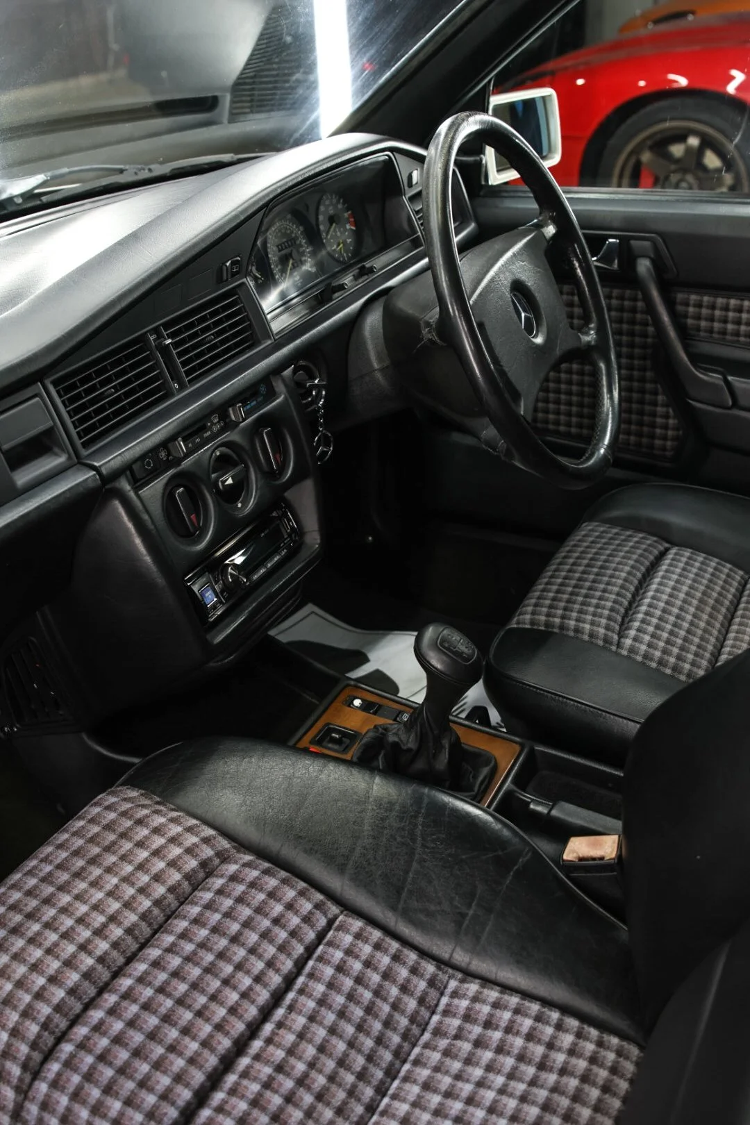 Interior of a vintage Mercedes-Benz car with plaid fabric seats, black dashboard, and manual gear shift.