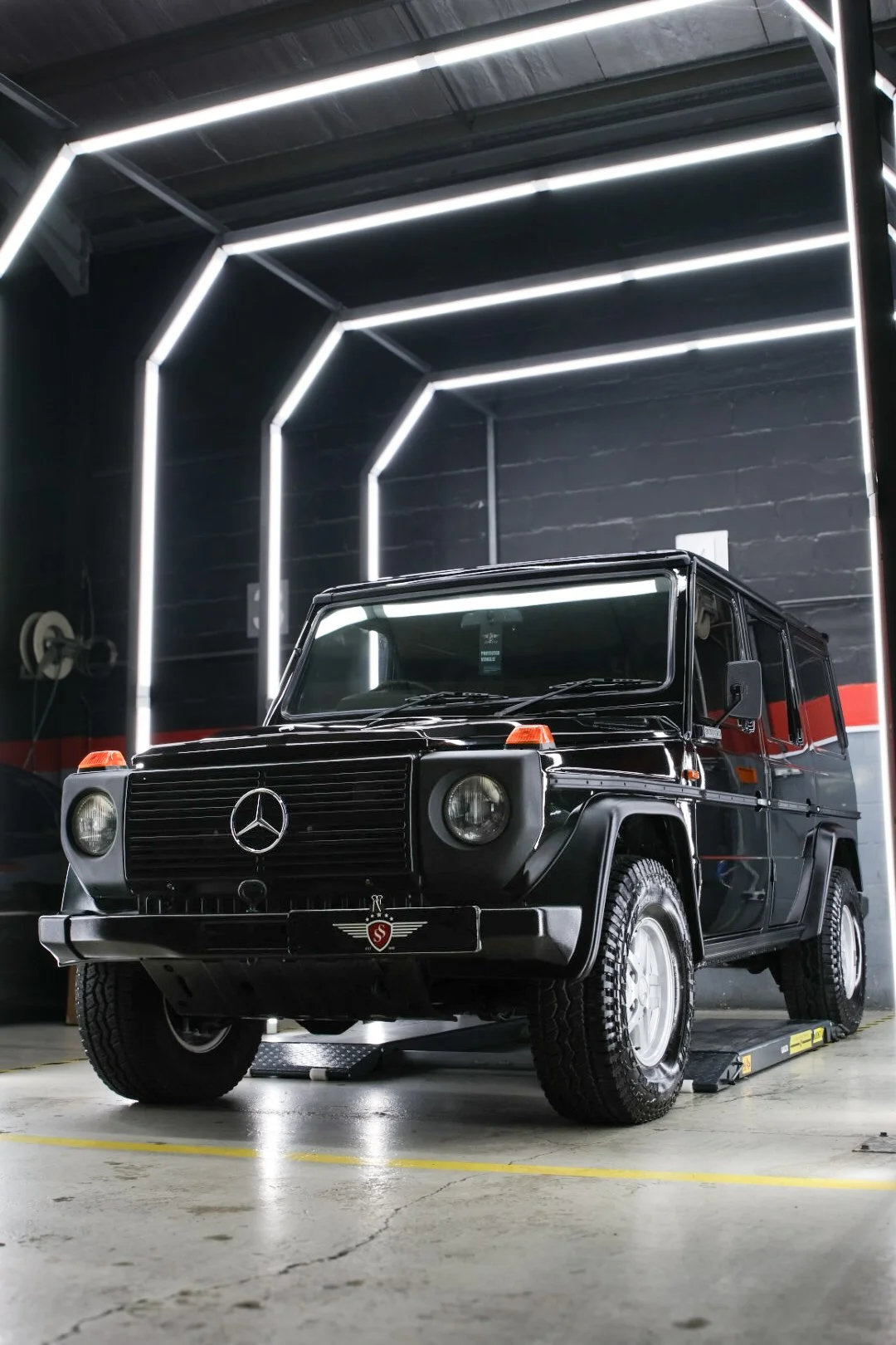 A black vintage Mercedes-Benz G-Class SUV parked inside a garage with modern LED strip lighting on the walls and ceiling.