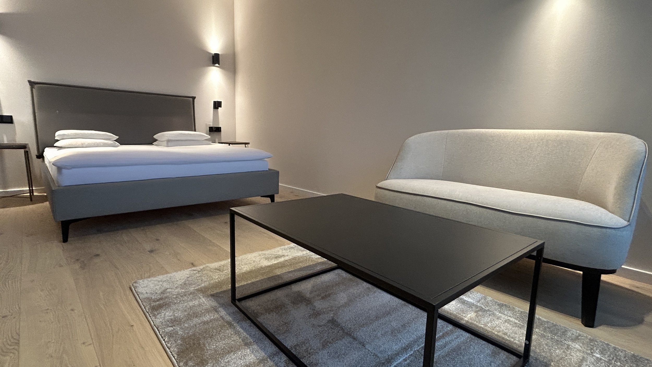 Modernes Schlafzimmer mit einem Bett, einem Sofa, einem Couchtisch und einem Teppich auf Holzboden.