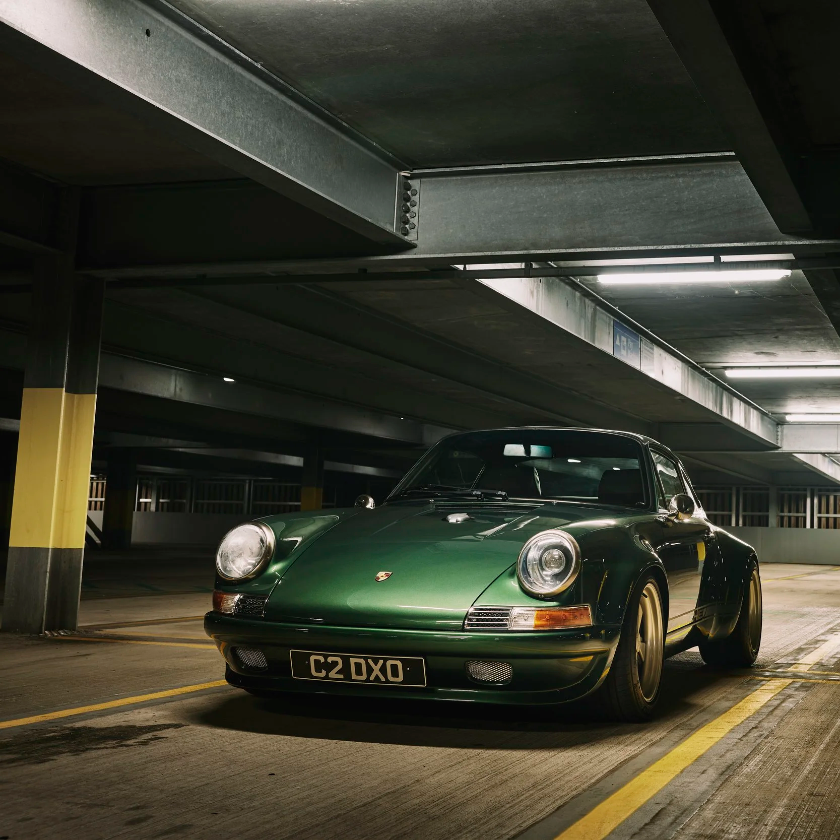 A classic green Porsche 911 parked in an underground parking garage with artificial lighting.