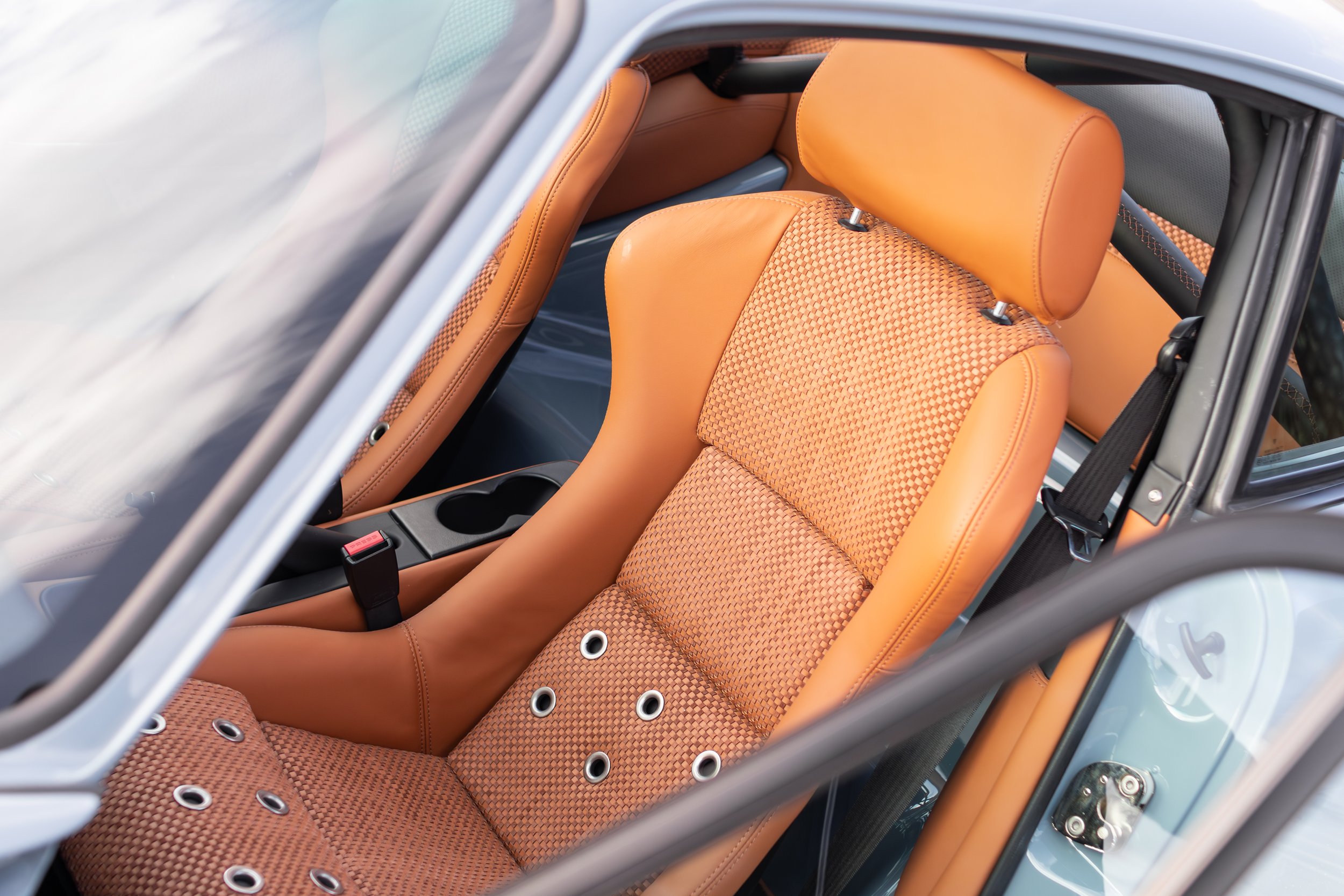 Interior of a car with tan leather and fabric seats, black seat belt, and a center console.