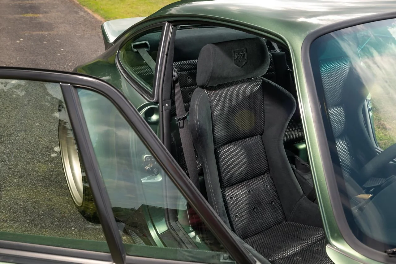 Close-up of the interior of a vintage green car, showing a racing bucket seat with black fabric upholstery.