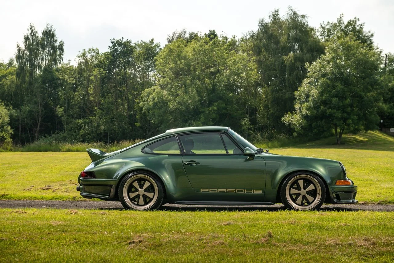Green vintage Porsche sports car parked on a grassy field with trees in the background.