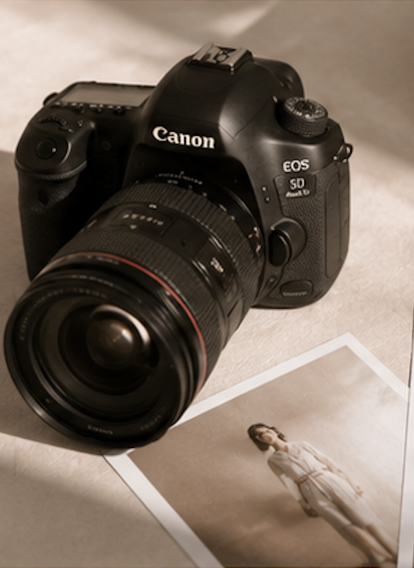 Una fotocamera Canon EOS con scheda SD e una fotografia di una donna in abito chiaro su uno sfondo neutro