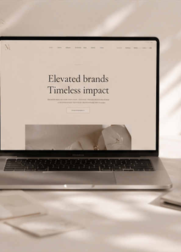 Schermo di un computer portatile con pagina web che afferma 'Elevated brands Timeless impact', posizionato su una scrivania con documenti e una penna.