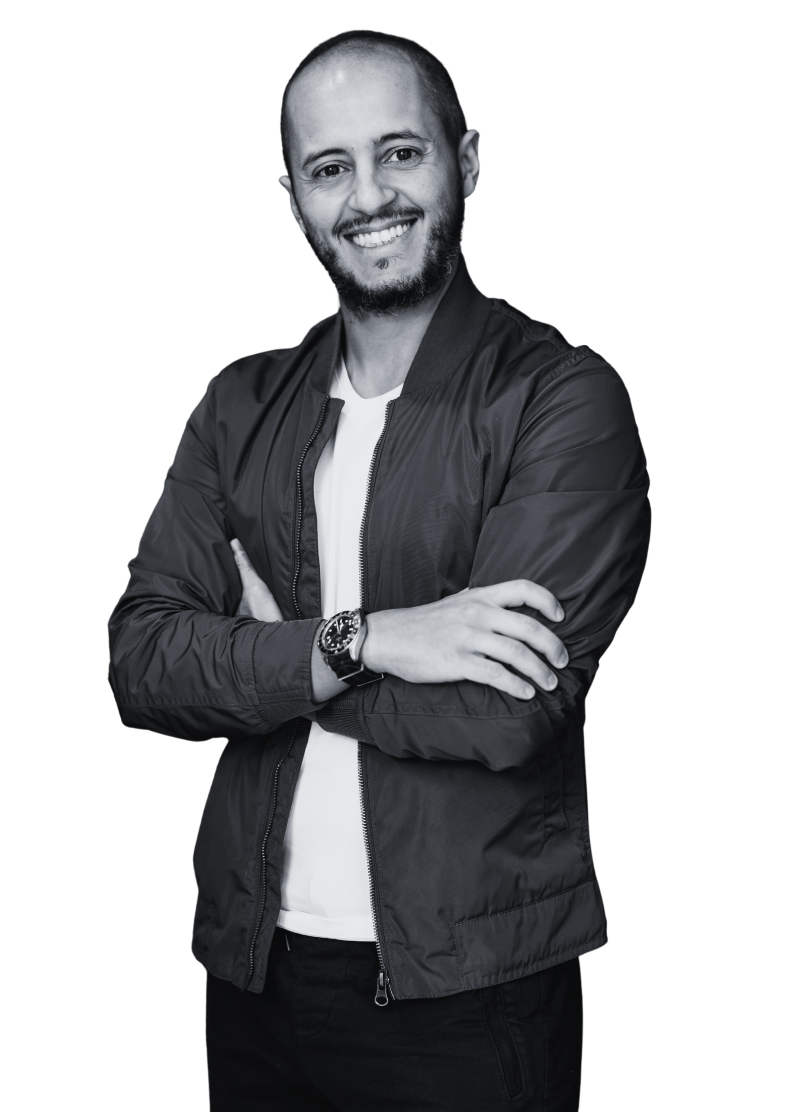 A smiling man with a beard and short hair, wearing a black jacket, white shirt, and a watch, standing with crossed arms on a dark background.