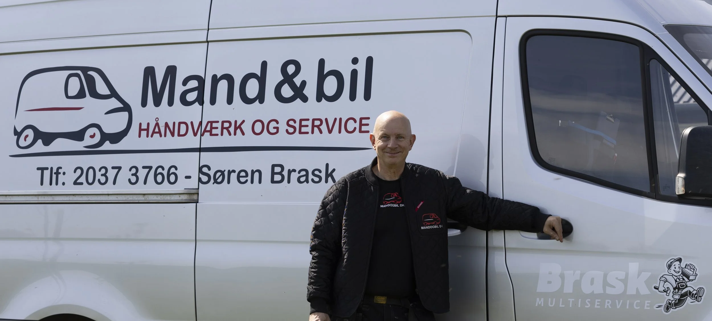 Mand står ved siden af en varevogn med logoet "Mand & bil Håndværk og Service" og kontaktinformationer.
