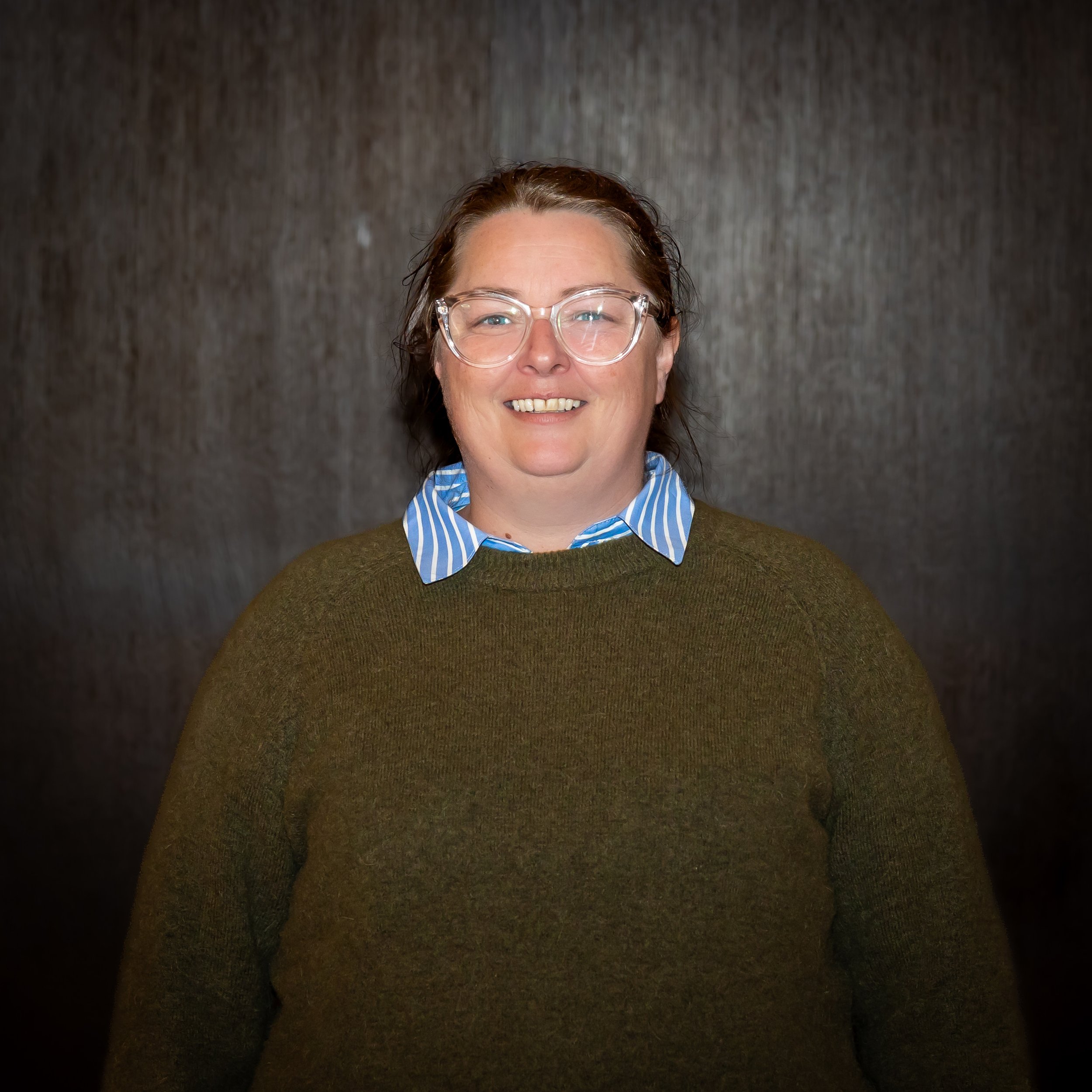 A woman with glasses and long brown hair smiling and holding a large bouquet of pink and white roses with greenery in a floral shop.