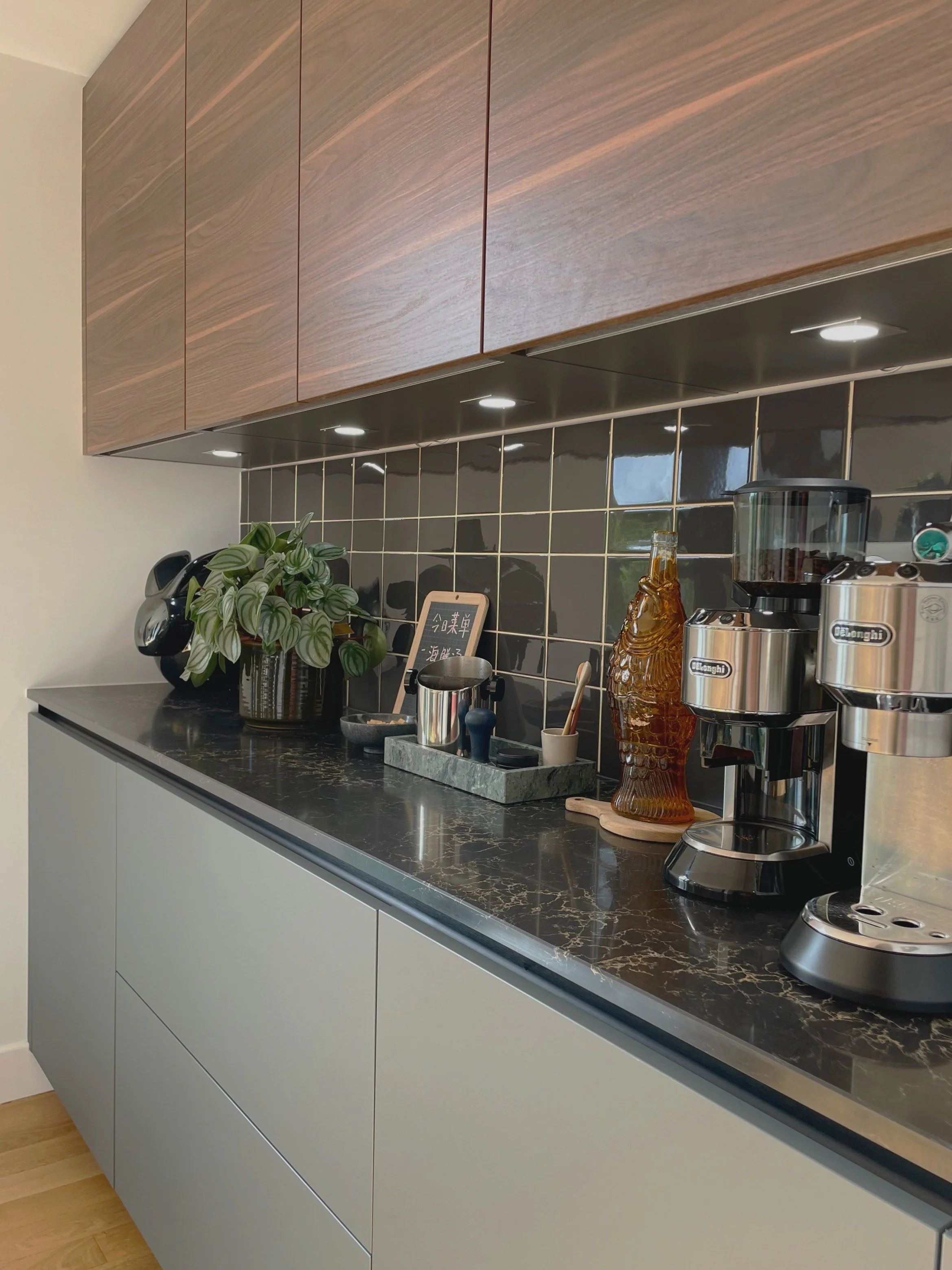 Cuisine moderne avec plan de travail en marbre noir, armoires en bois, machine à café, plantes et éclairage intégré.