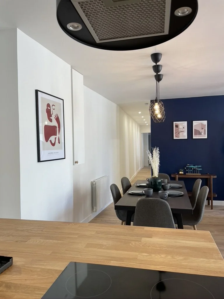 Salle à manger moderne avec table en bois, chaise, décoration murale et luminaires suspendus.